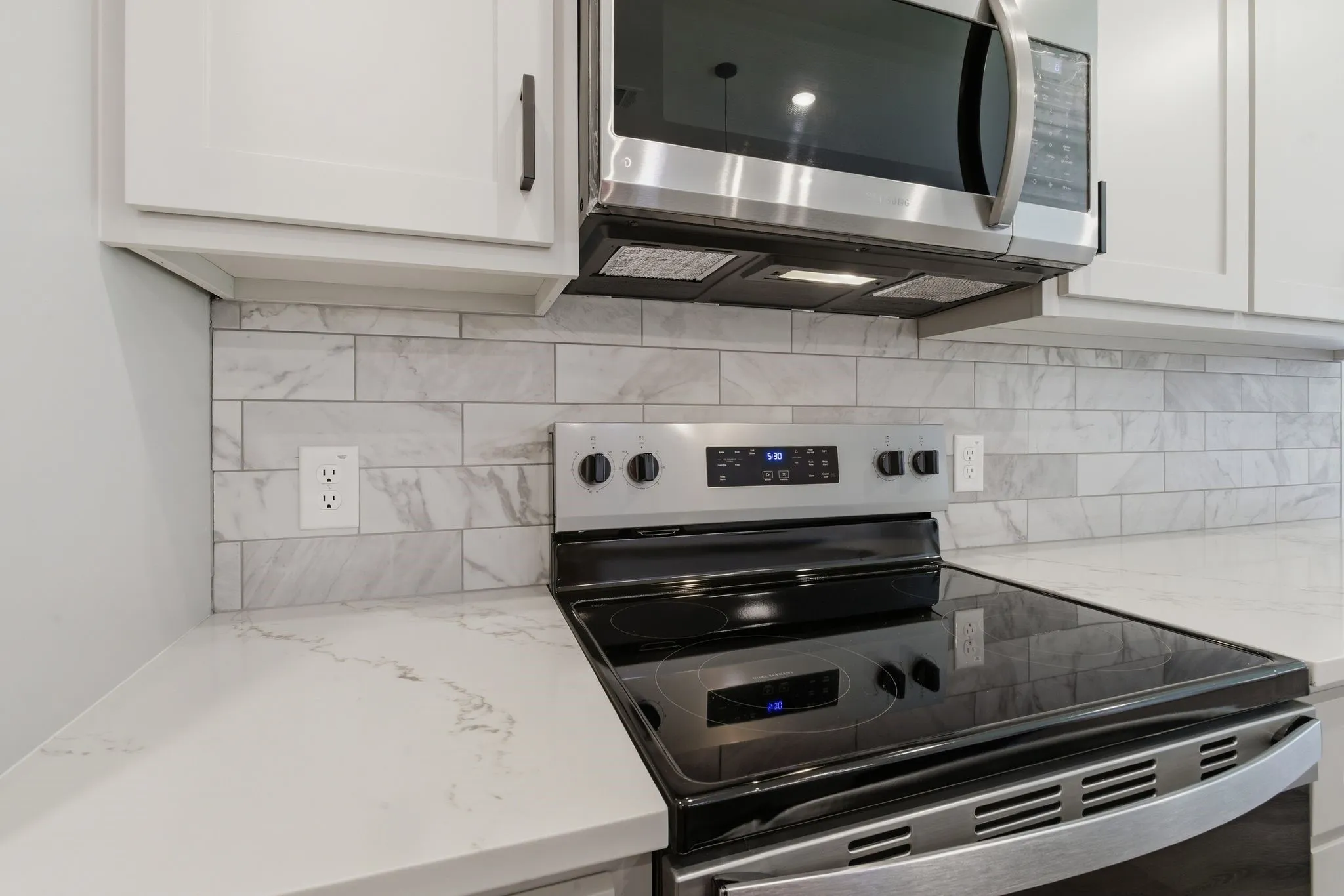 White cabinetry with dark hardware, subway tile backsplash, light-toned countertop, stainless steel microwave, and stainless steel range