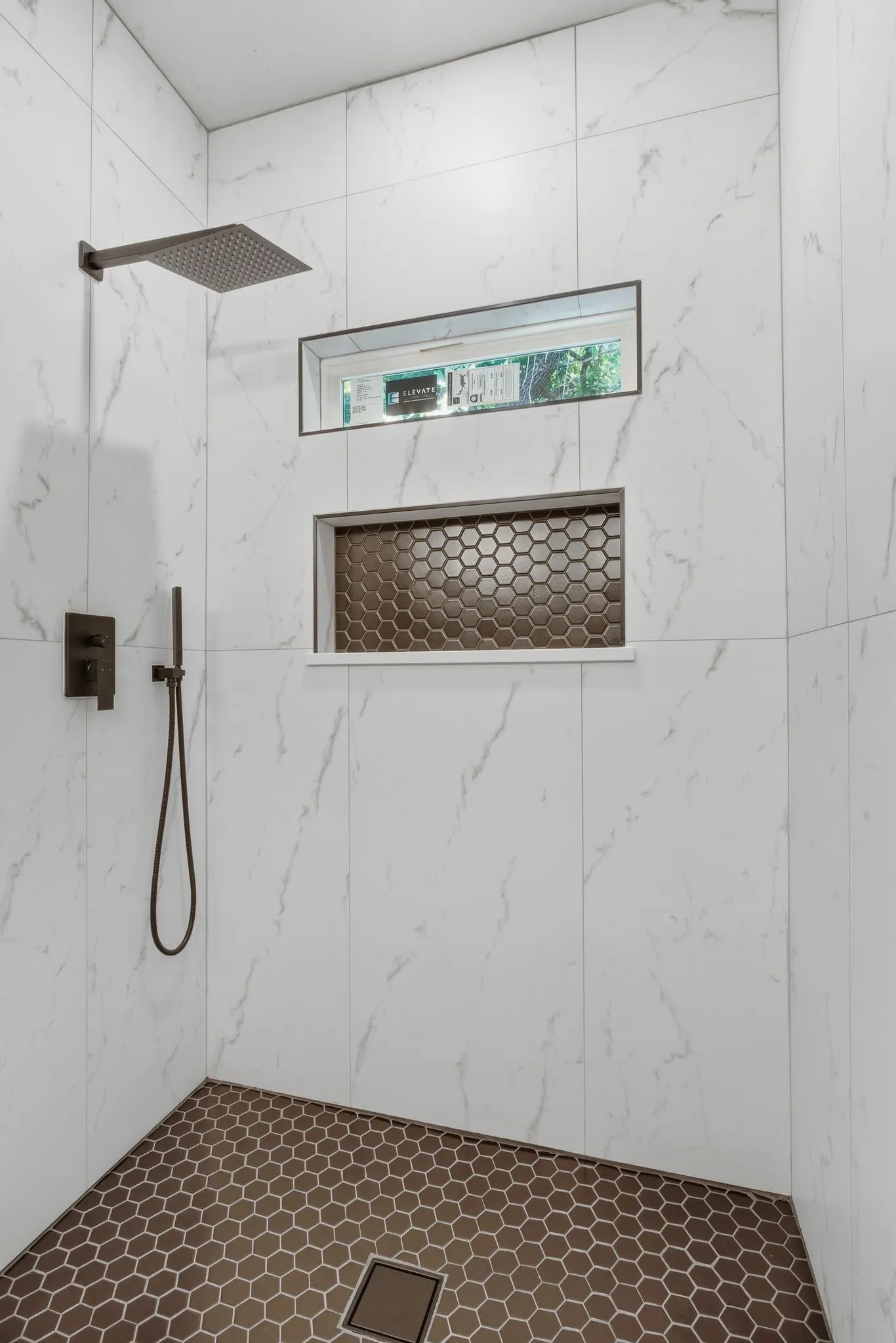 Shower stall featuring white marble-look wall tiles, a rainfall showerhead, and a coordinating handheld shower