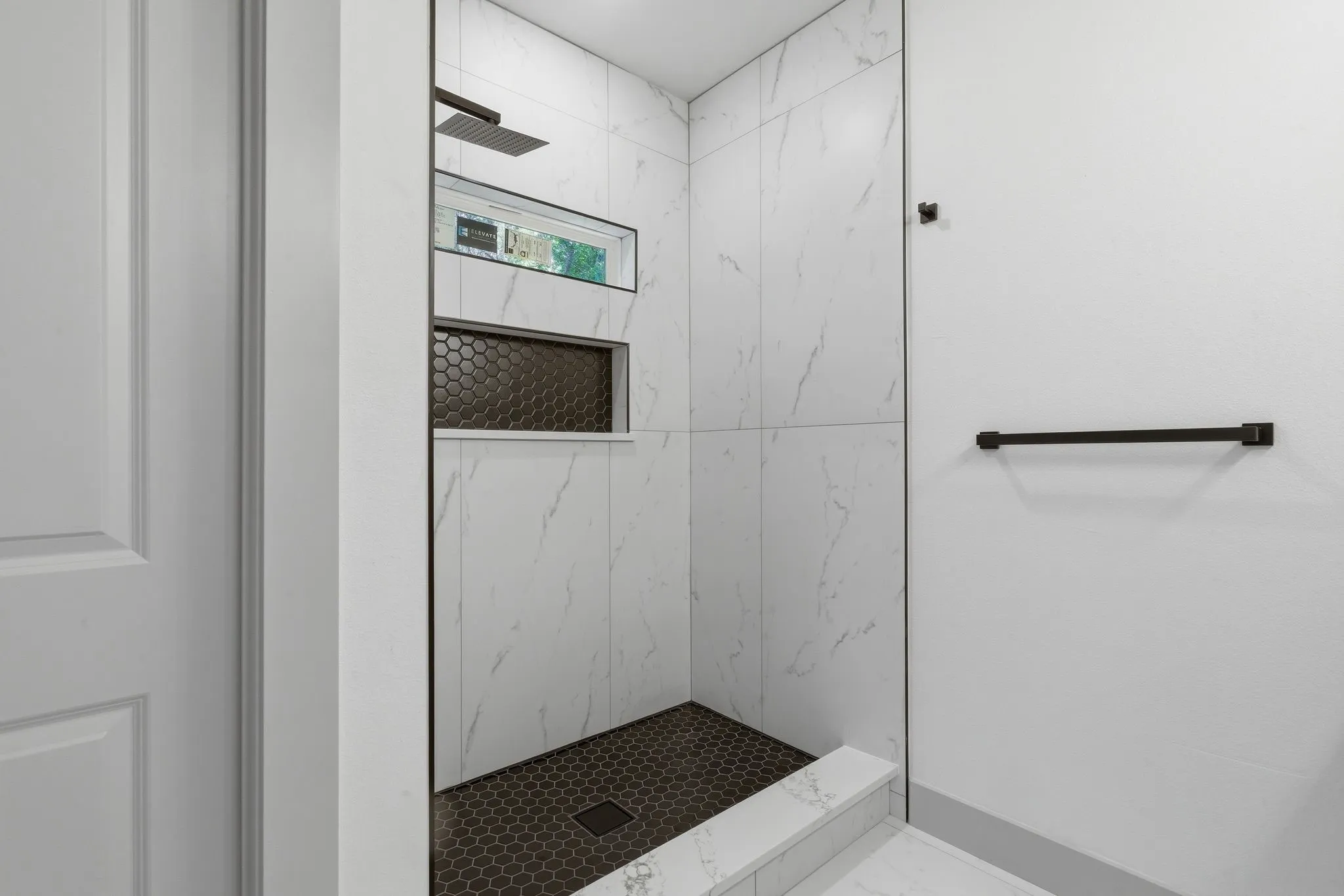 Shower with white marble-look tile, dark hexagonal floor tile, dual built-in shower niches, and a rainfall showerhead