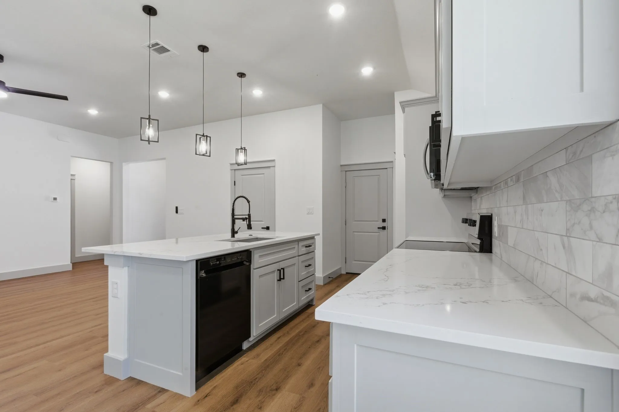 Kitchen featuring a large island with sink, white countertops, built-in dishwasher, light gray cabinetry, and a white subway tile backsplash
