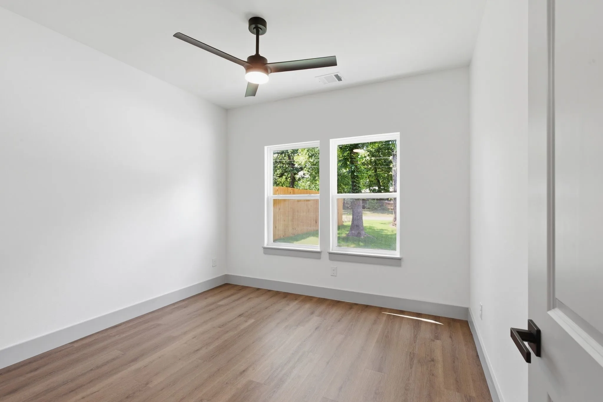 Bright interior space featuring wood-finish flooring, a modern ceiling fan, and two windows