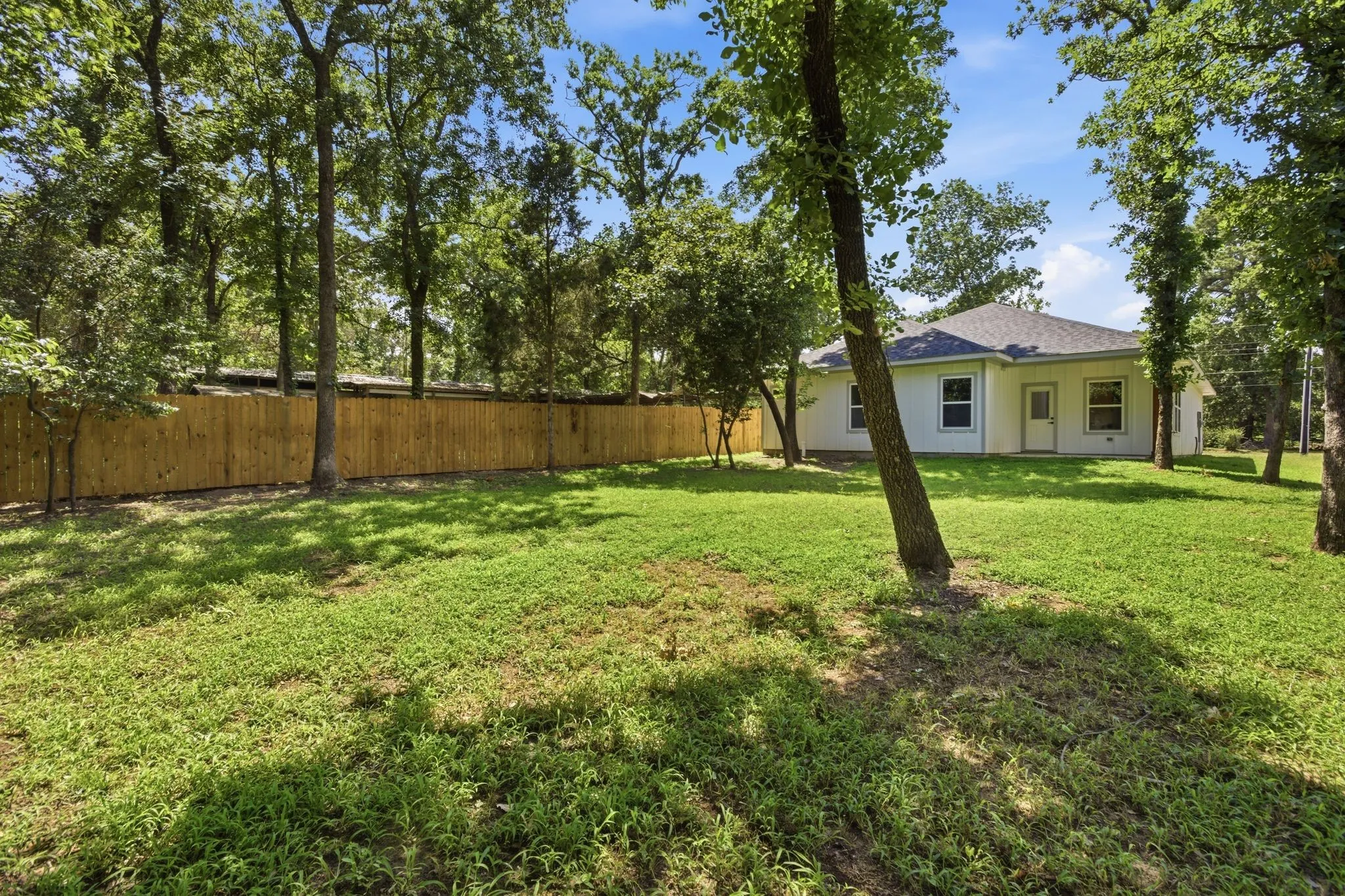 Expansive backyard featuring a new wood privacy fence, mature trees, and a white exterior residence with multiple windows and a shingled roof