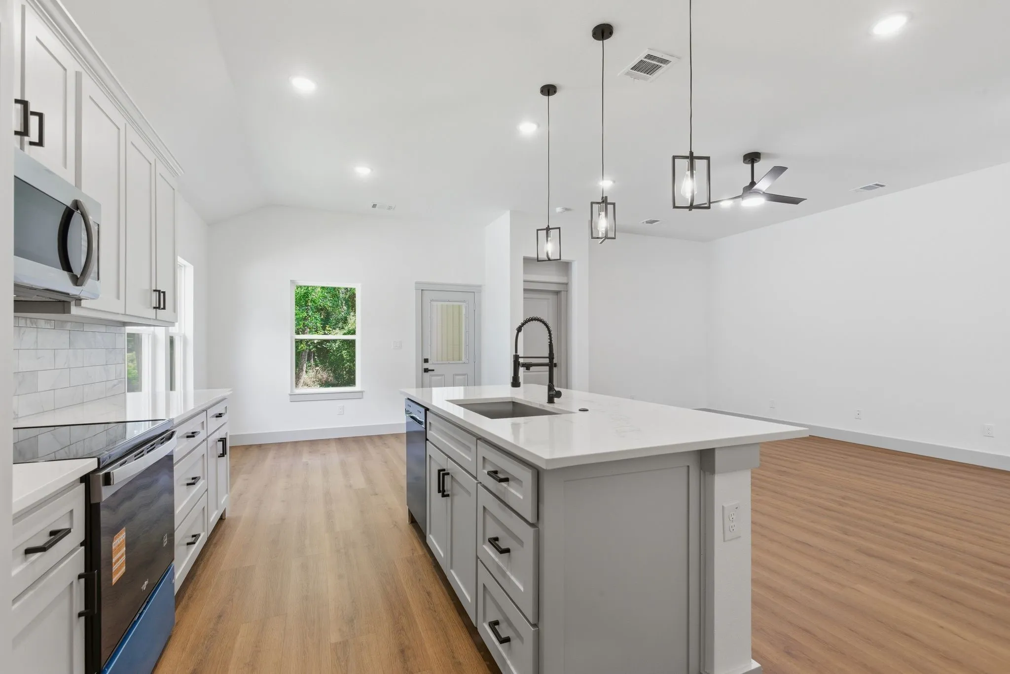Modern kitchen featuring light cabinetry, stainless steel appliances, a center island with sink, and wood-finish flooring