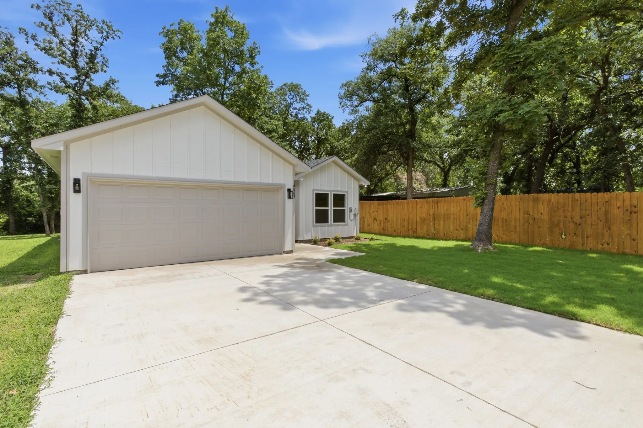 White board and batten siding, attached two-car garage with light gray door, concrete driveway, and natural wood privacy fence