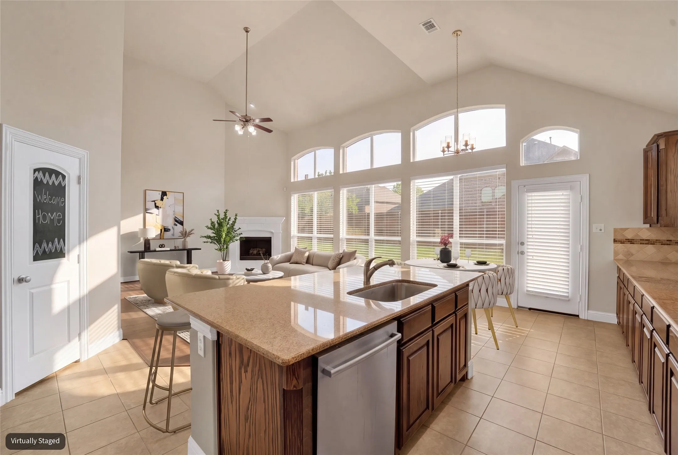 Vaulted ceiling, arched windows, kitchen island with integrated sink, stainless steel dishwasher, and tiled flooring