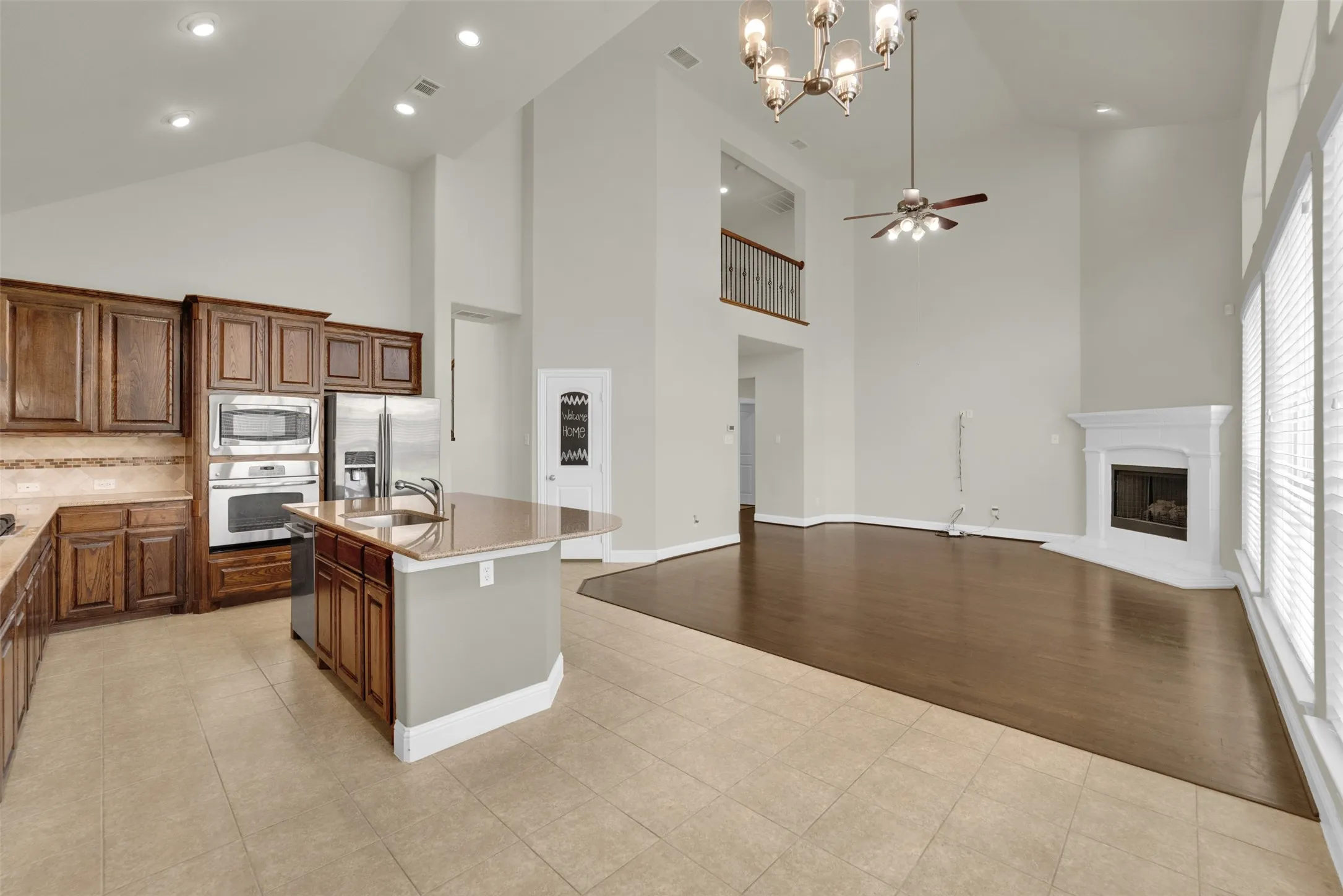 Vaulted ceilings with recessed lighting, wood-finish flooring, a kitchen island with a sink, built-in stainless steel appliances, and a fireplace with a mantel