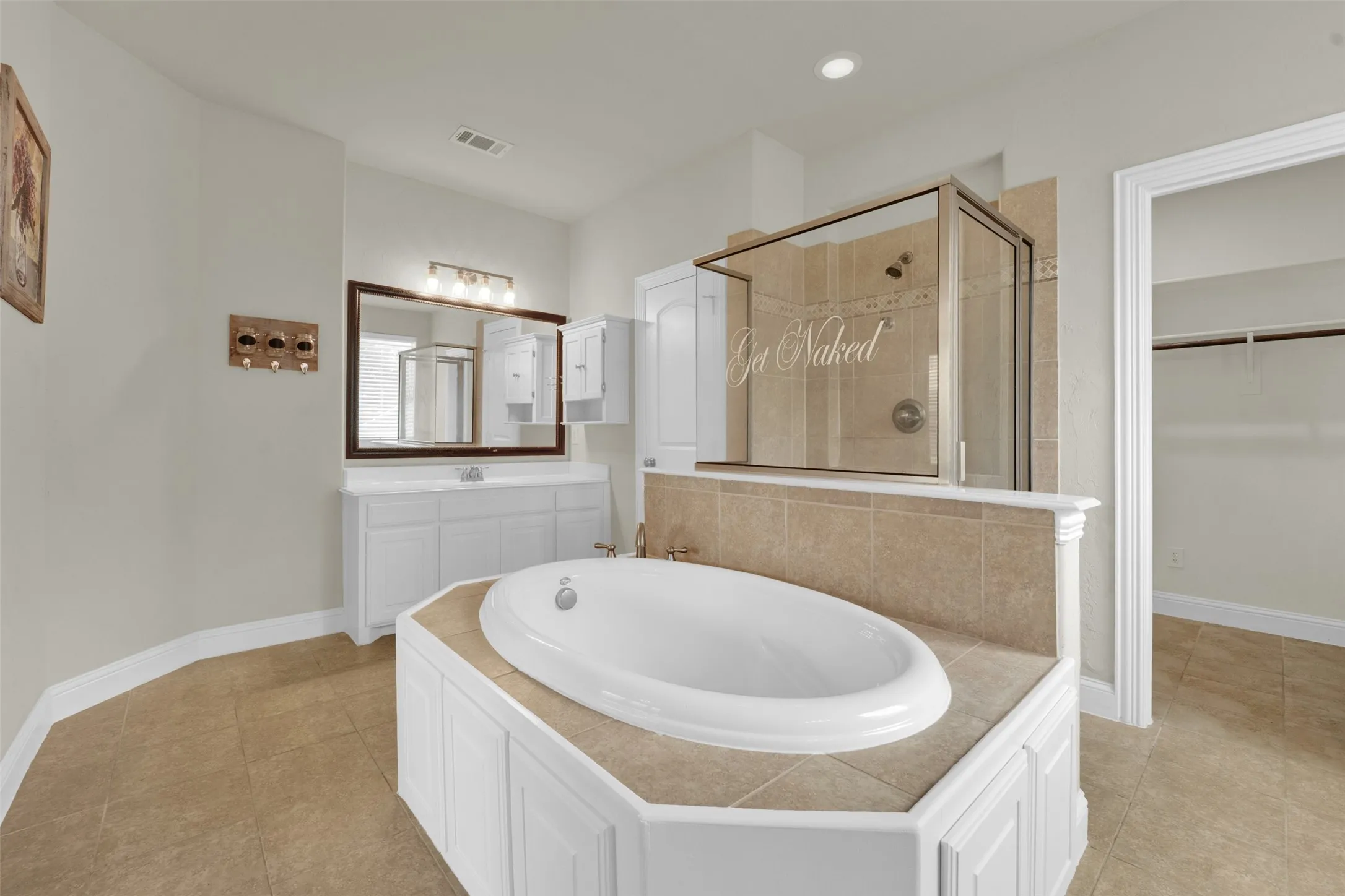 Soaking tub with tiled surround, glass-enclosed shower, single vanity with integrated sink, large wall mirror, and tile flooring