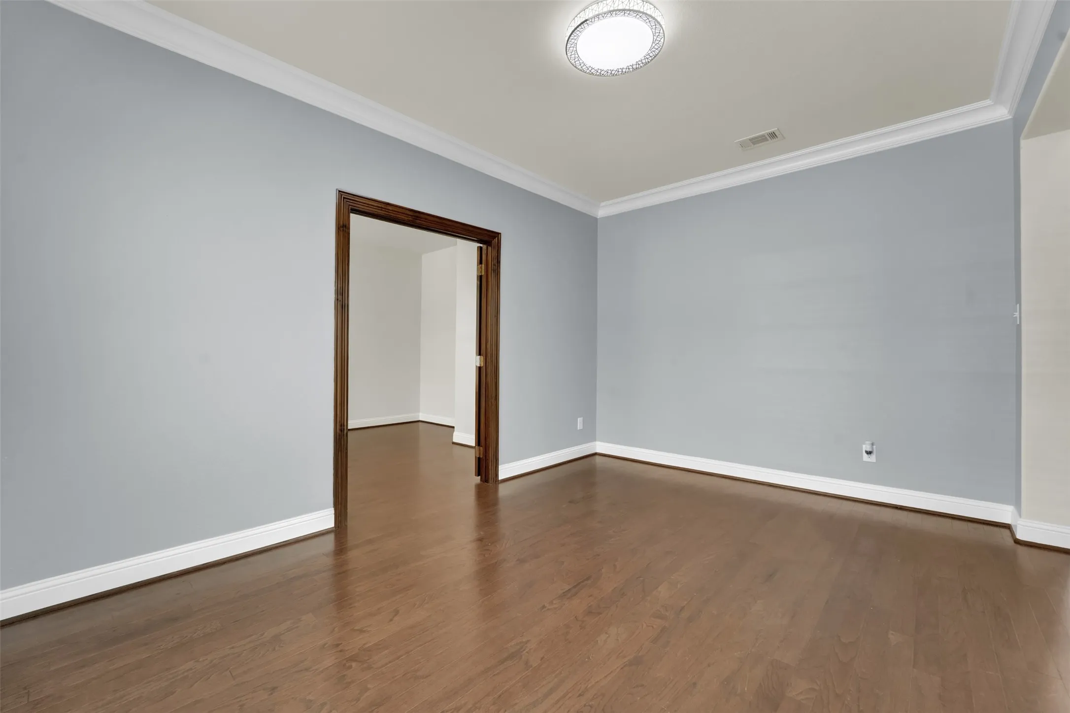 Wood-finish flooring, crown molding, a recessed entryway, and a flush-mount ceiling light