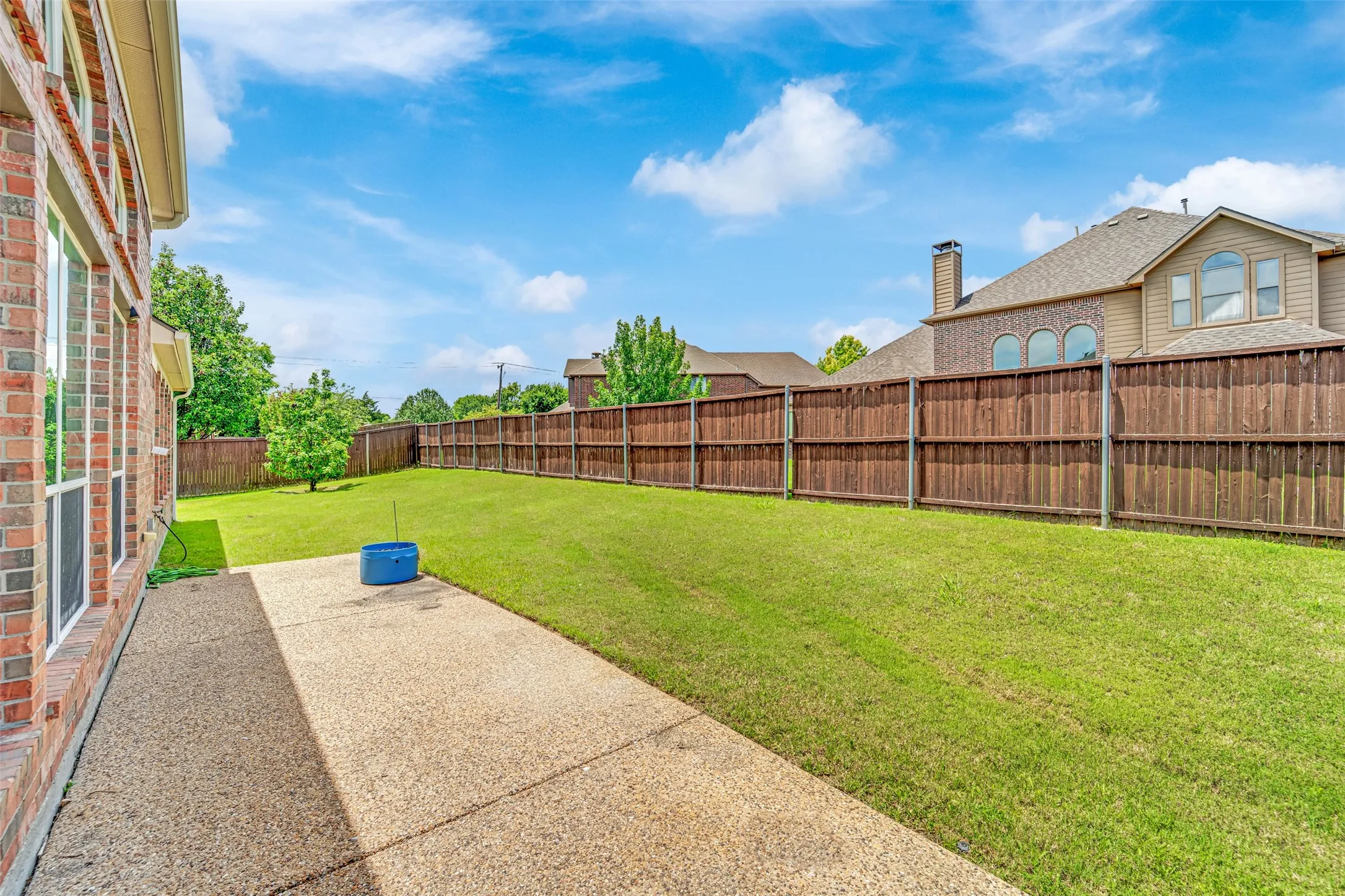 Expansive green lawn, wood privacy fencing, concrete patio, and brick exterior with multiple windows