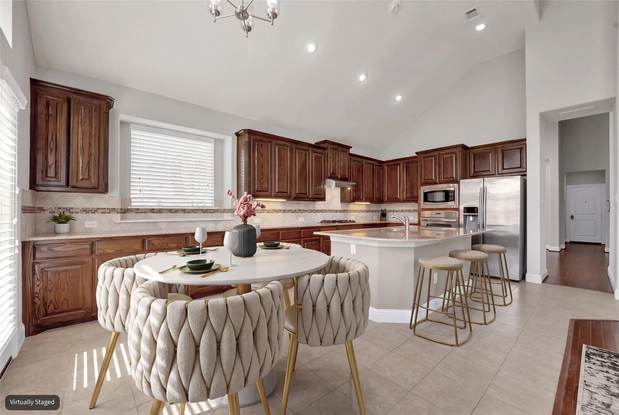 Spacious kitchen with vaulted ceilings, recessed lighting, wood cabinetry, stainless steel appliances, and a central island with bar seating