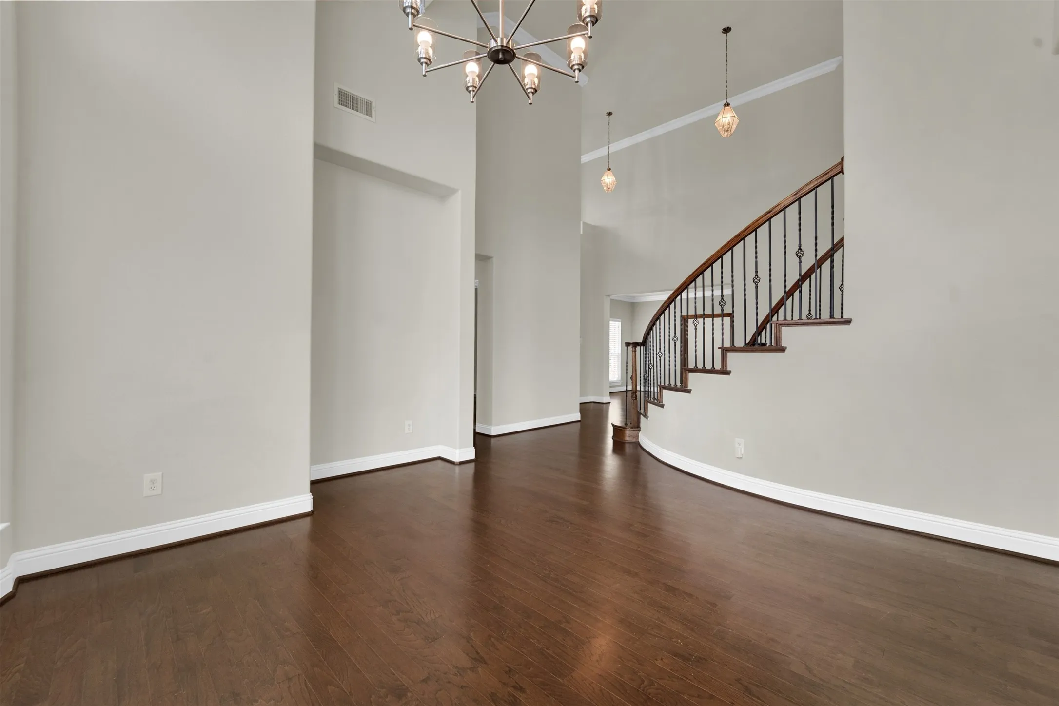 Dark wood-finish flooring, a curved staircase with wrought iron balusters, high ceilings, and crown molding