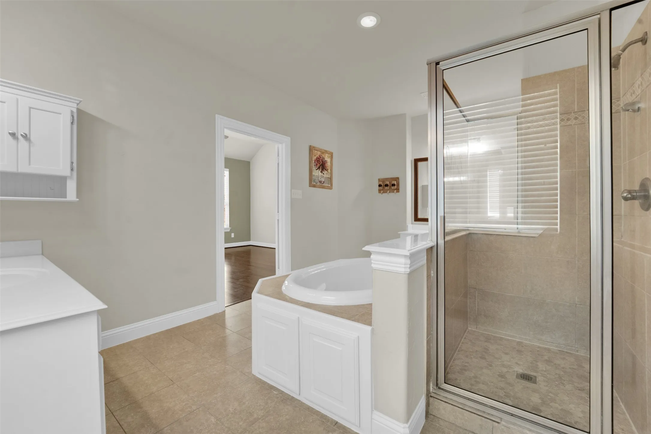 Tiled flooring, white vanity with integrated sink, built-in soaking tub, glass-enclosed shower, and recessed lighting