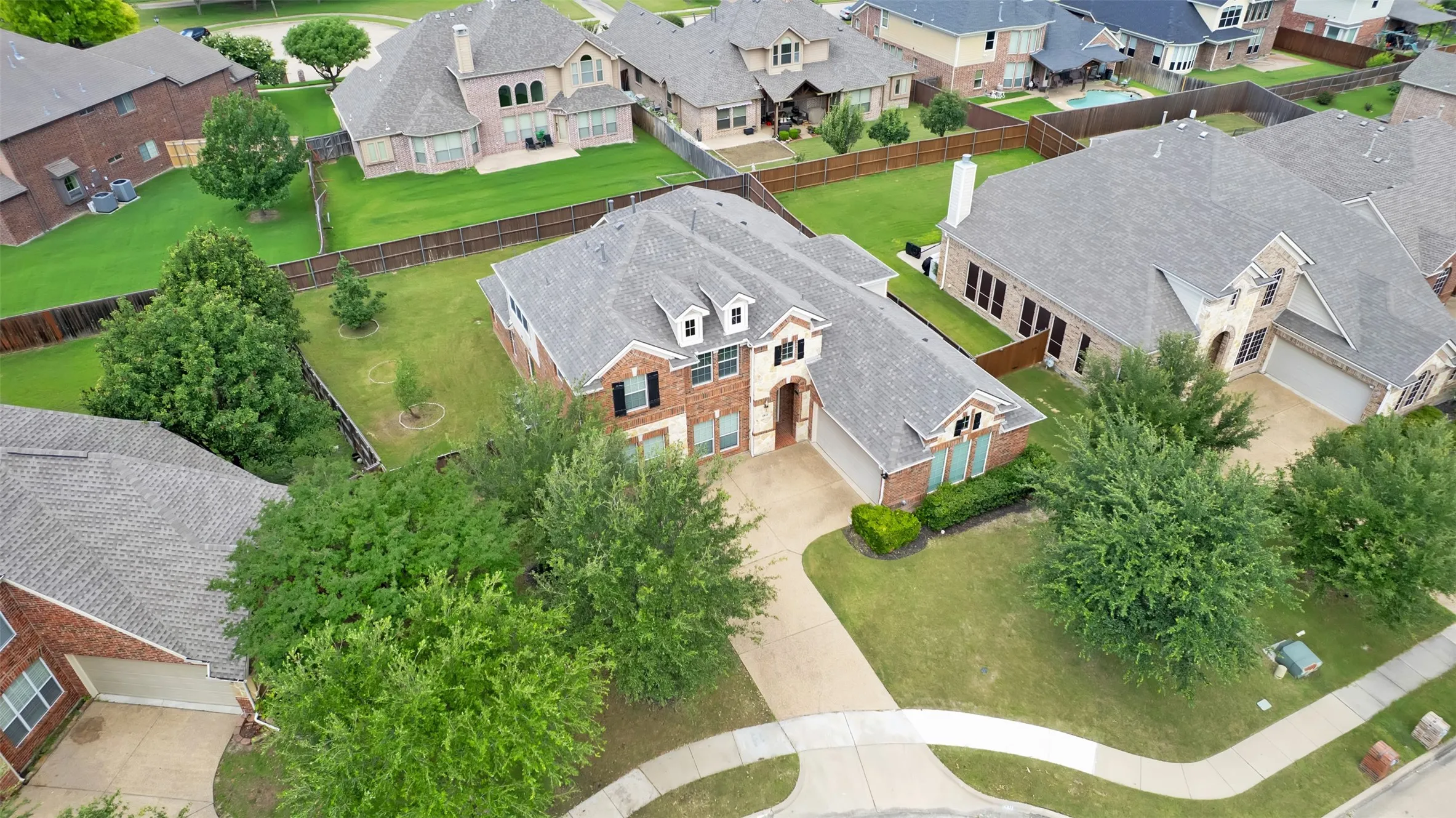 Brick and stone facade, dormer windows, attached two-car garage, mature landscaping, and a concrete driveway