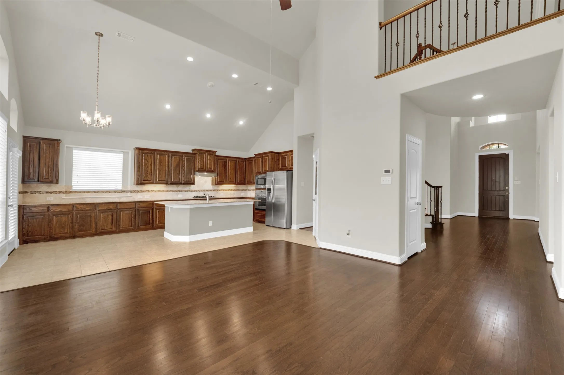 Two-story ceiling, recessed lighting, wood-finish flooring, wood cabinetry, and a kitchen island