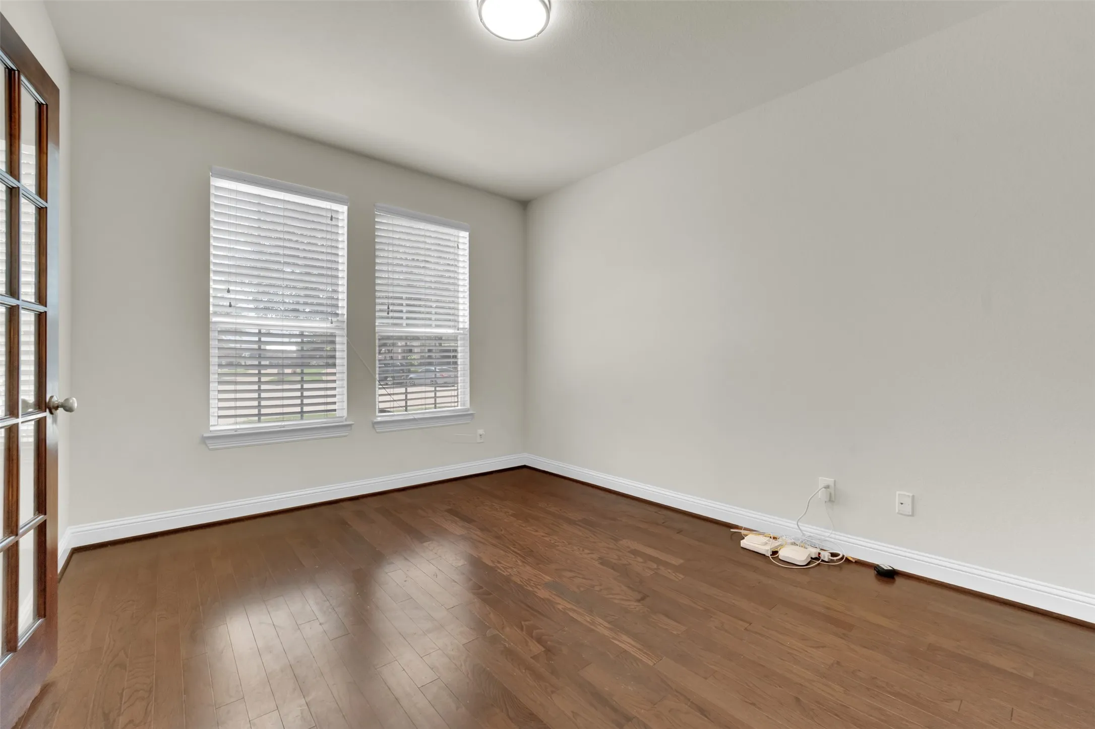 Wood-finish flooring, two windows with blinds, and a paneled door