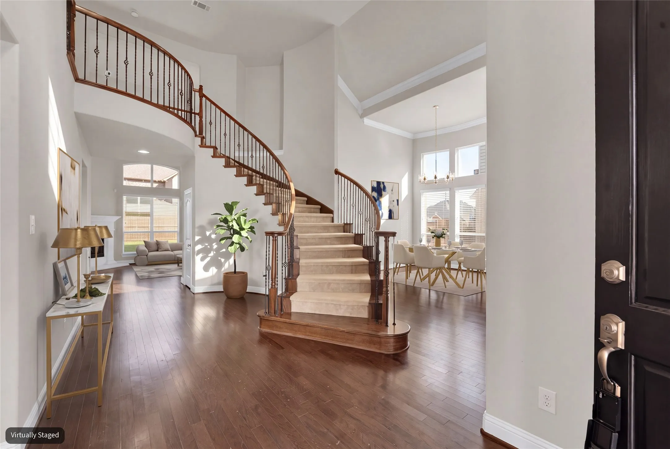 Grand foyer featuring a curved staircase with wrought iron balusters and wood handrails, hardwood flooring, and tall windows