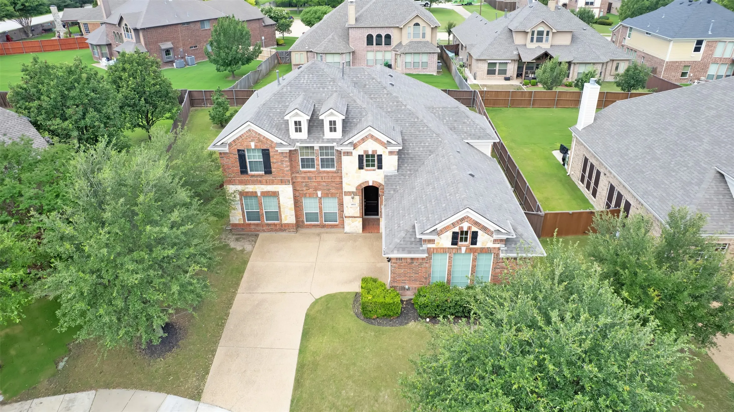 Brick and stone facade, dormer windows, attached two-car garage, concrete driveway, and mature landscaping