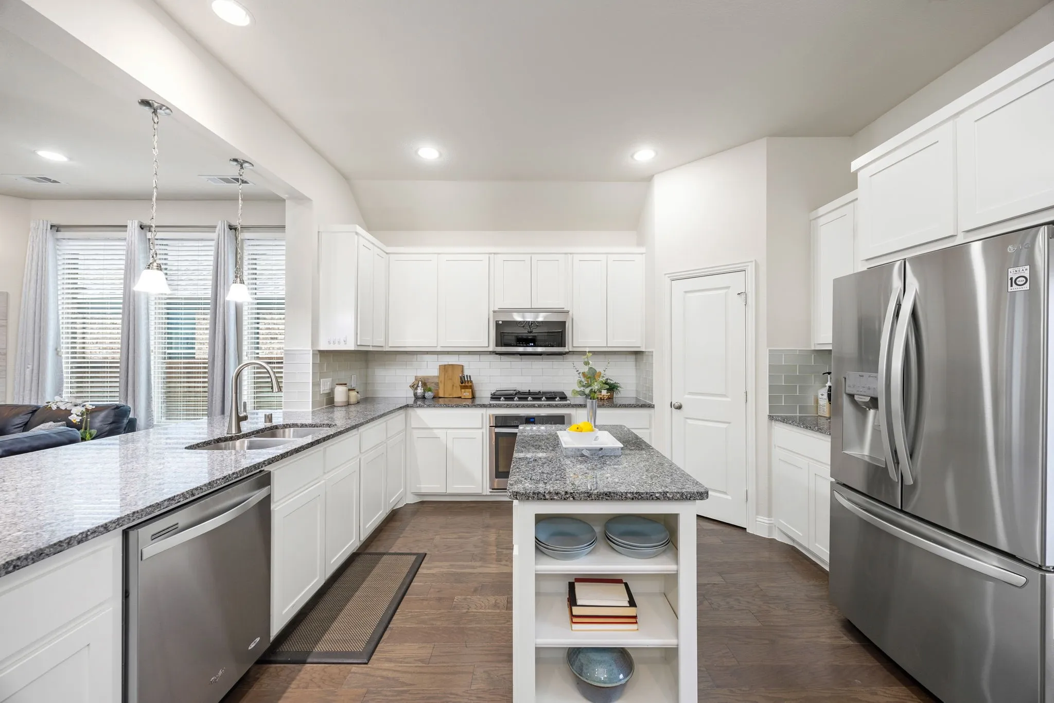 Modern kitchen featuring white cabinetry, stainless steel appliances, a center island with built-in shelving, durable wood-finish flooring, and recessed lighting