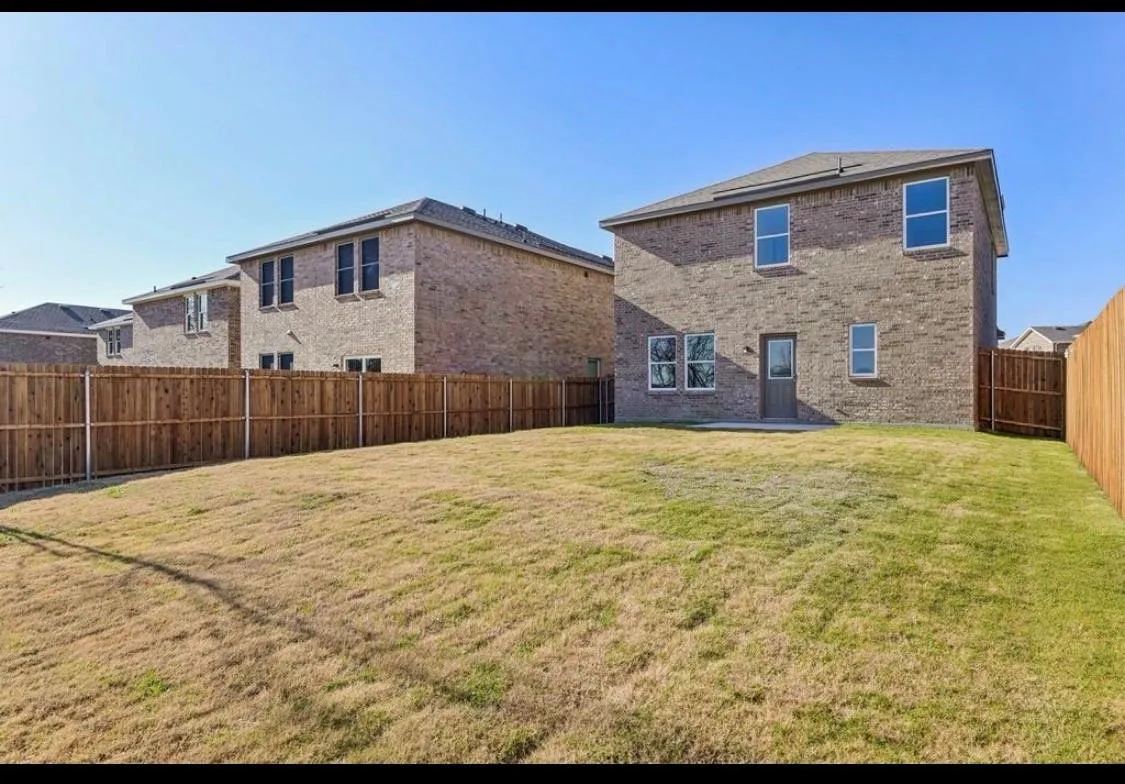 Expansive backyard with a full privacy fence, brick exterior, and a ground-level patio