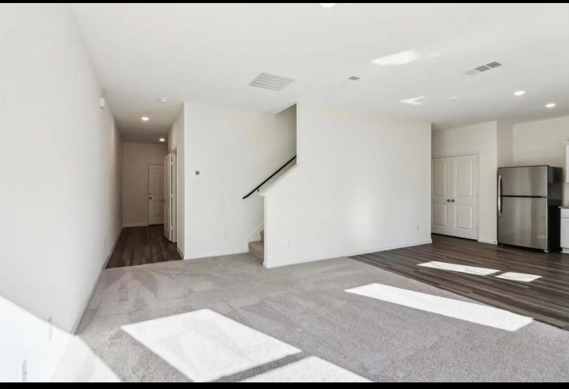 Open-concept living area featuring carpet and wood-finish flooring, recessed lighting, and a kitchen area with a stainless steel refrigerator