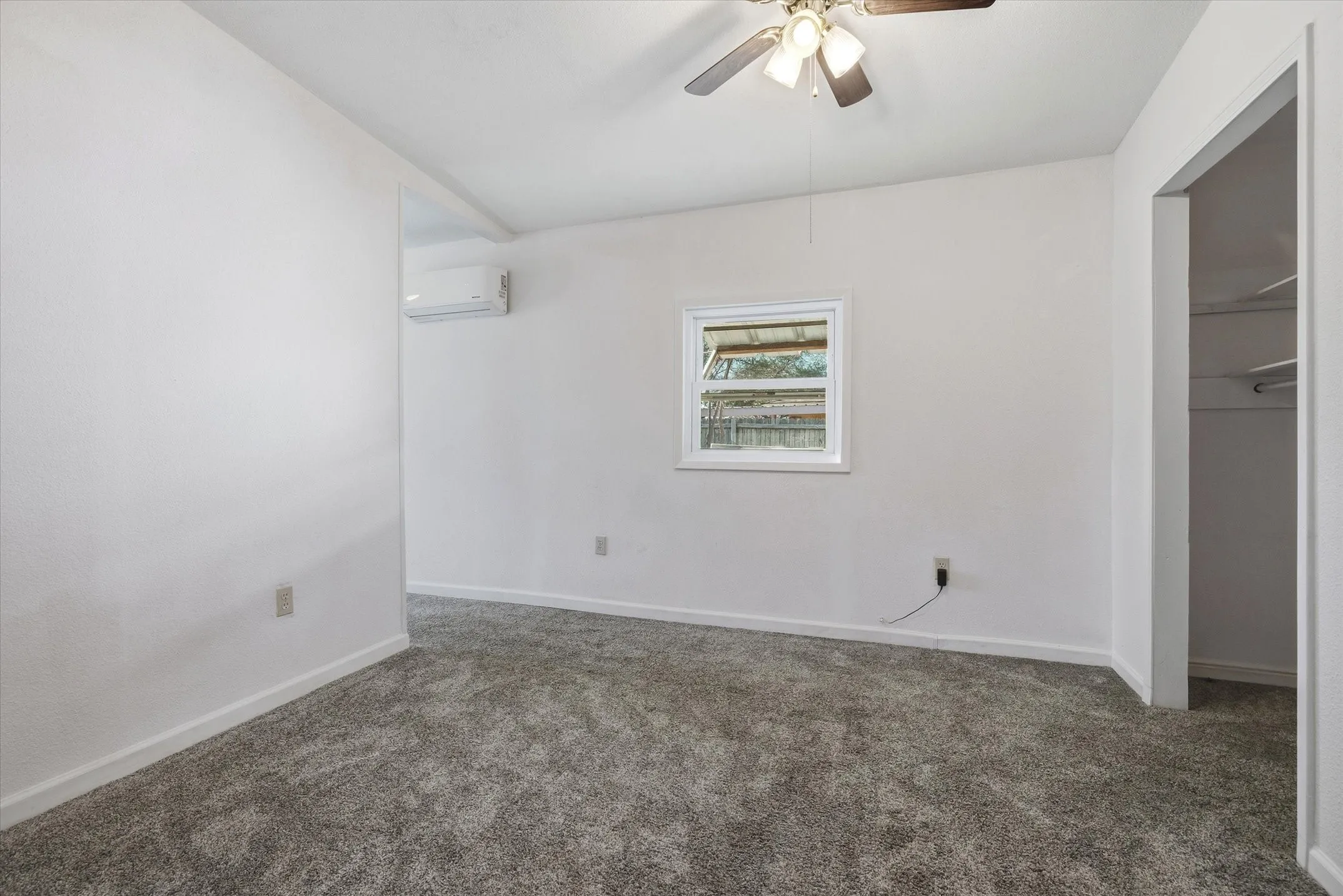 Carpeted interior with a ceiling fan, wall-mounted air conditioning unit, and a window