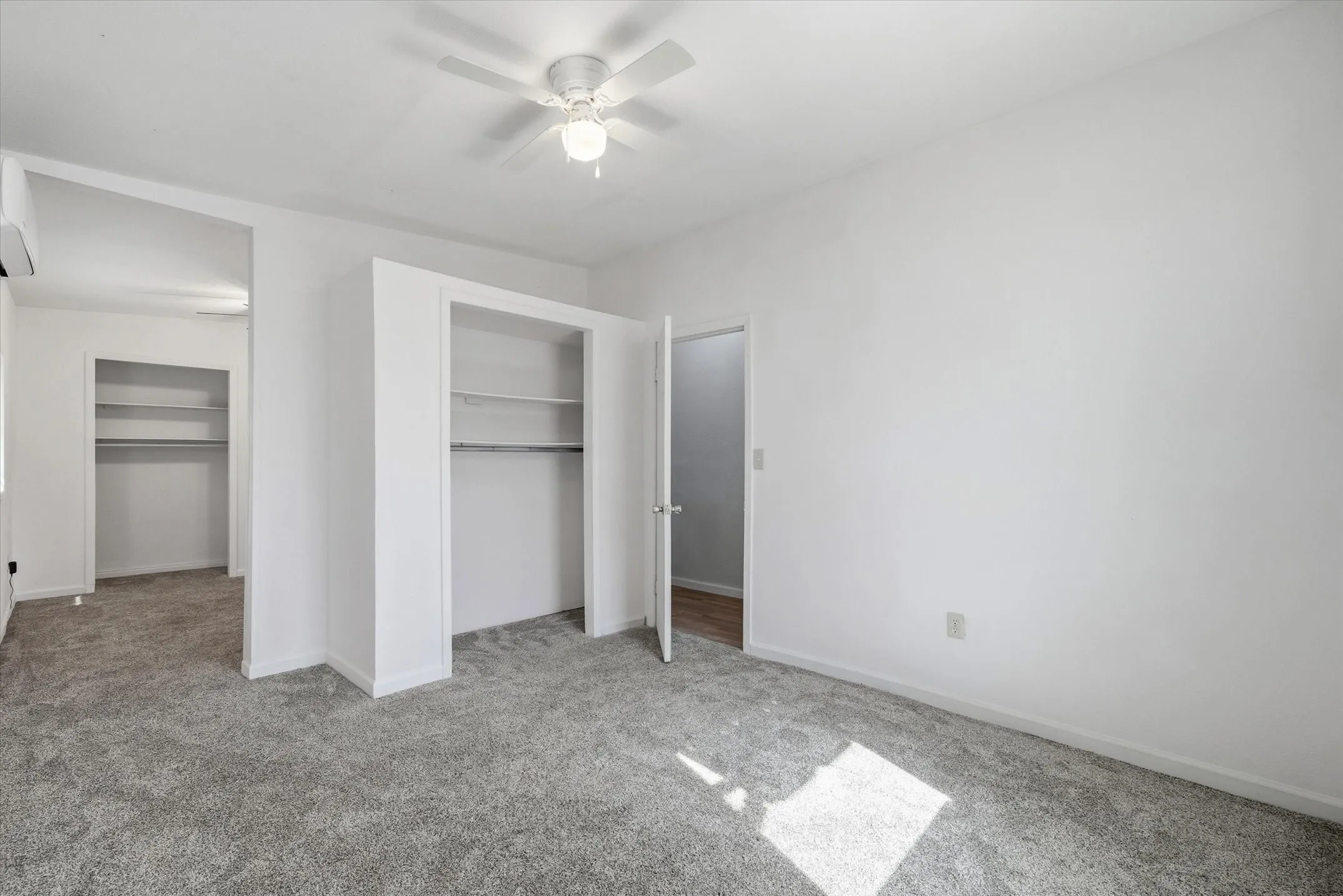 Wall-to-wall carpeting, dual built-in closets with shelving, ceiling fan, and white walls