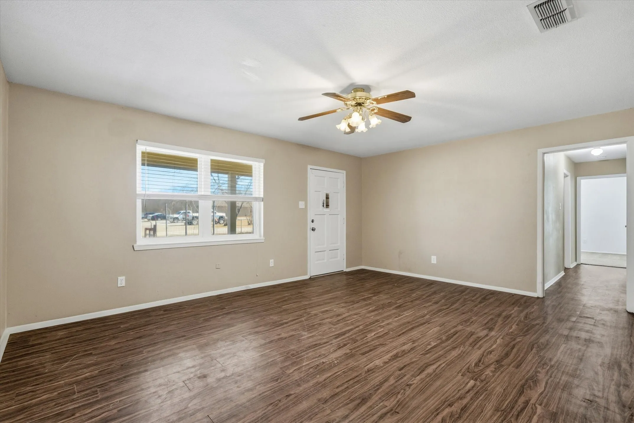 Wood-finish flooring, neutral wall paint, ceiling fan light fixture, and a white paneled entry door