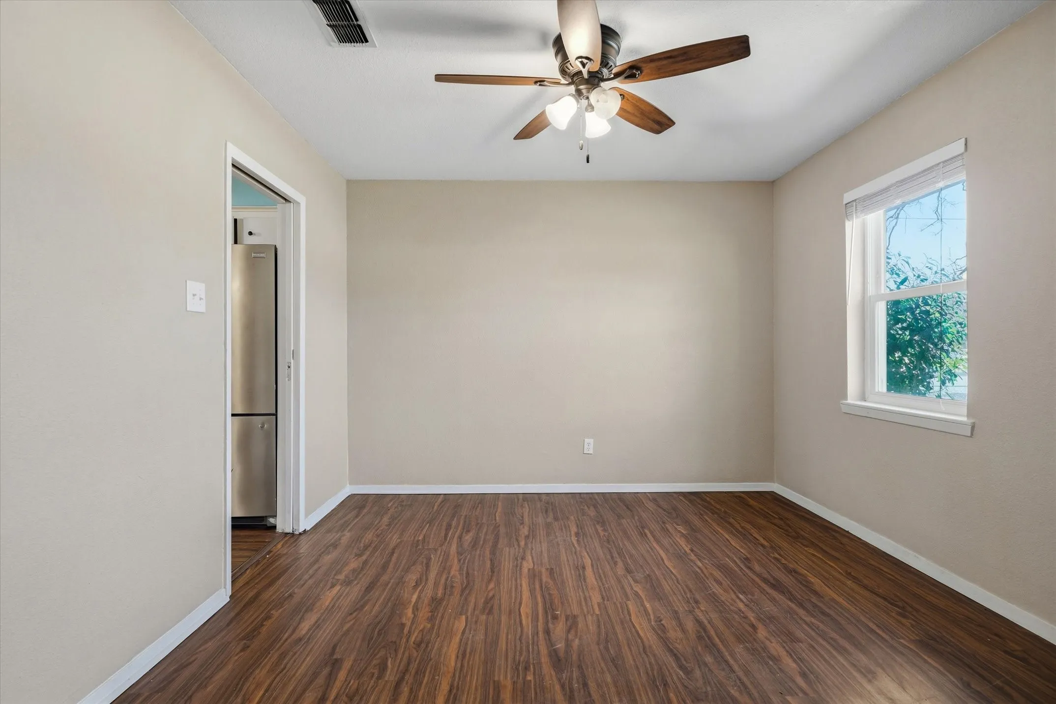 Room featuring wood-finish flooring, a ceiling fan with light fixture, and a window with white trim