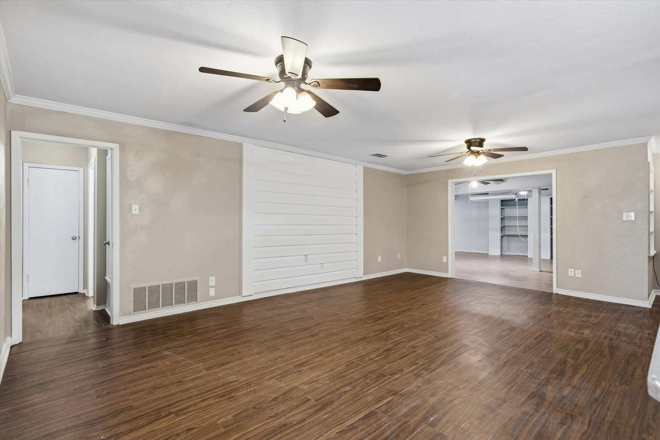 Spacious room featuring wood-finish flooring, two ceiling fans, and a white shiplap accent wall