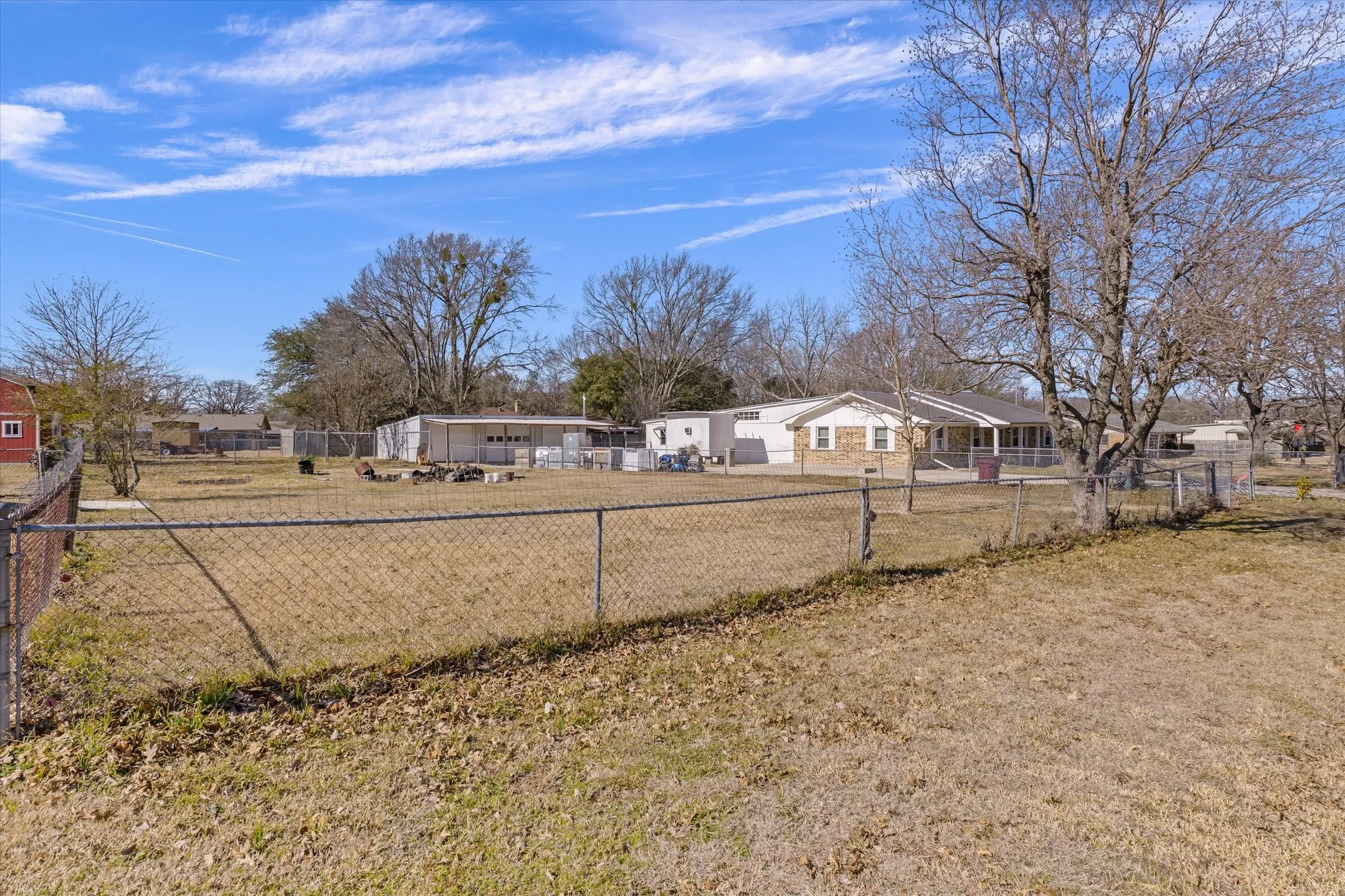 Expansive property featuring a chain-link fence, mature trees, and a residential structure with a covered porch