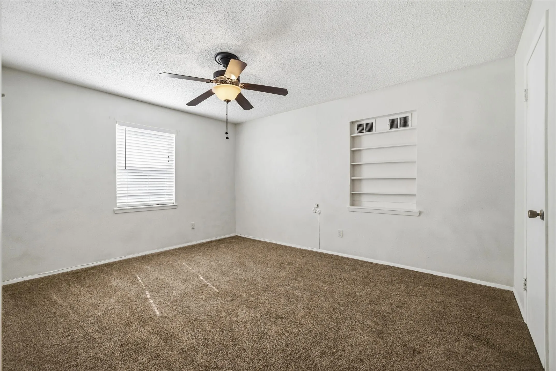 Recessed shelving, ceiling fan with integrated lighting, carpeted flooring, window with blinds, and a white paneled door
