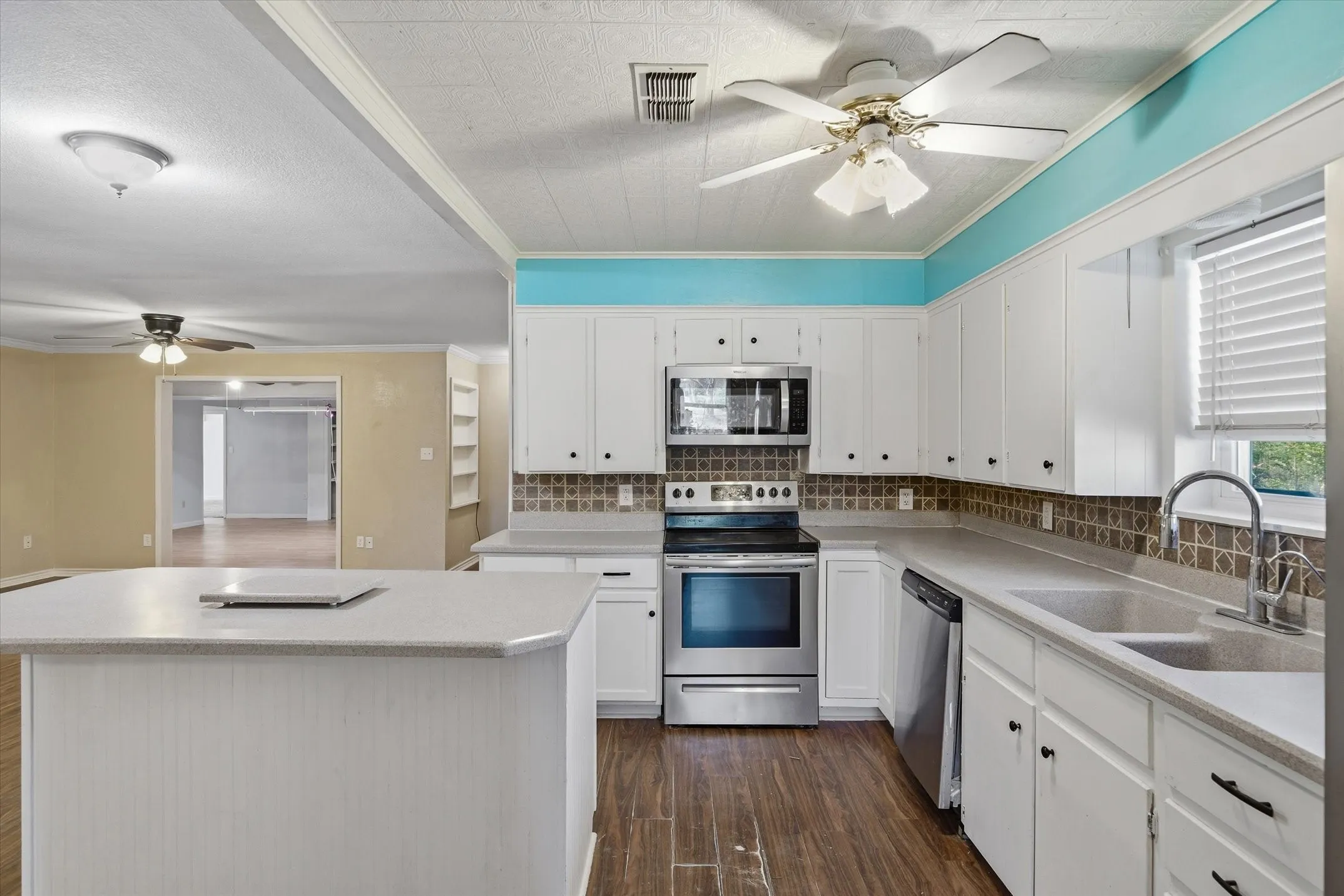 Kitchen featuring white cabinetry, stainless steel appliances, wood-finish flooring, a tiled backsplash, and a large island