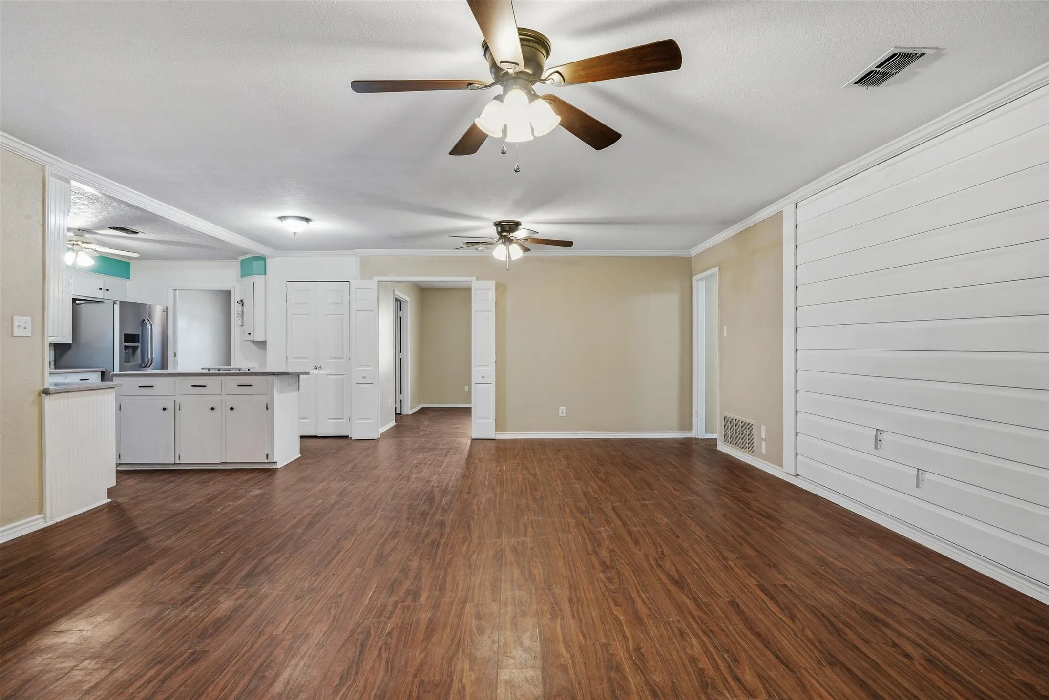 Wood-finish flooring throughout, white paneled wall accent, ceiling fans, recessed lighting, and white cabinetry in the kitchen area