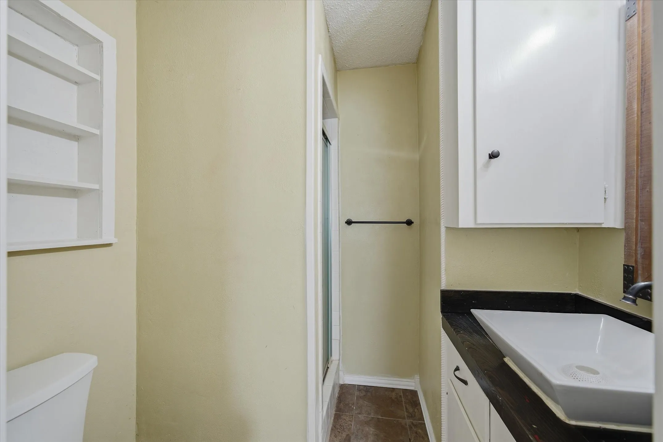 Built-in shelving, white vanity cabinetry with black hardware, dark countertop, white vessel sink, and an enclosed shower stall