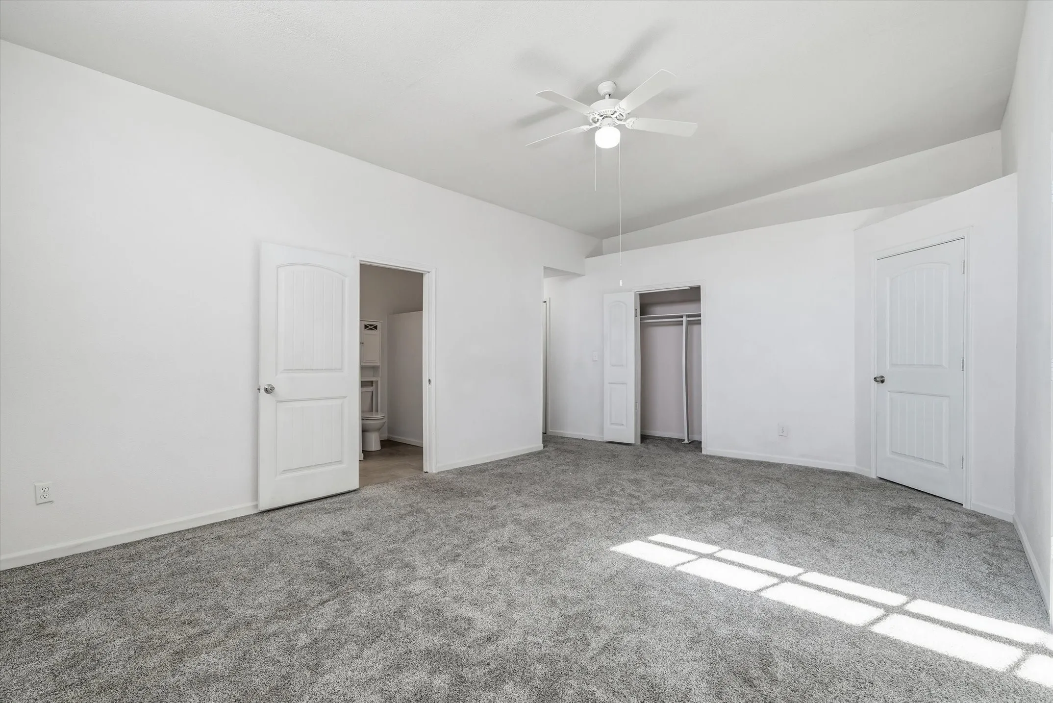 Spacious room featuring vaulted ceilings, a ceiling fan with integrated lighting, soft gray carpeting, and white paneled doors