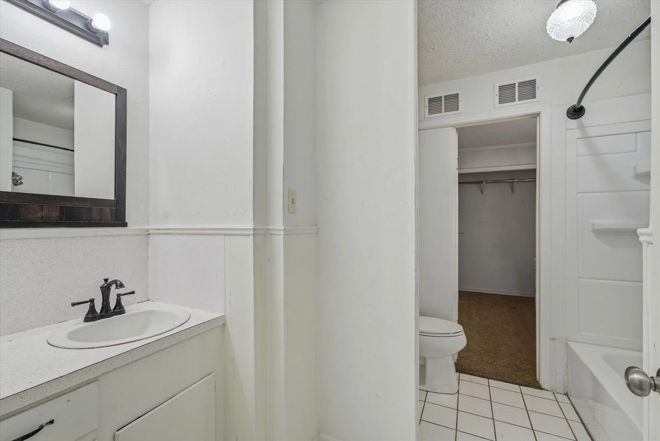 Bathroom featuring a vanity with an integrated sink, a dark framed mirror, white wainscoting, and white tiled flooring