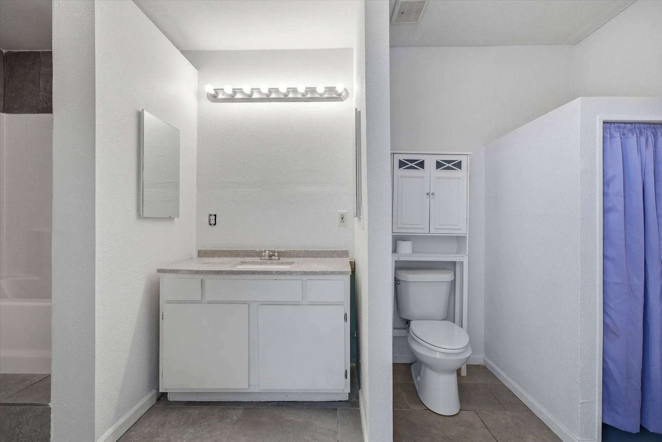 Vanity with a light-colored countertop, wall-mounted mirror, and cabinet storage