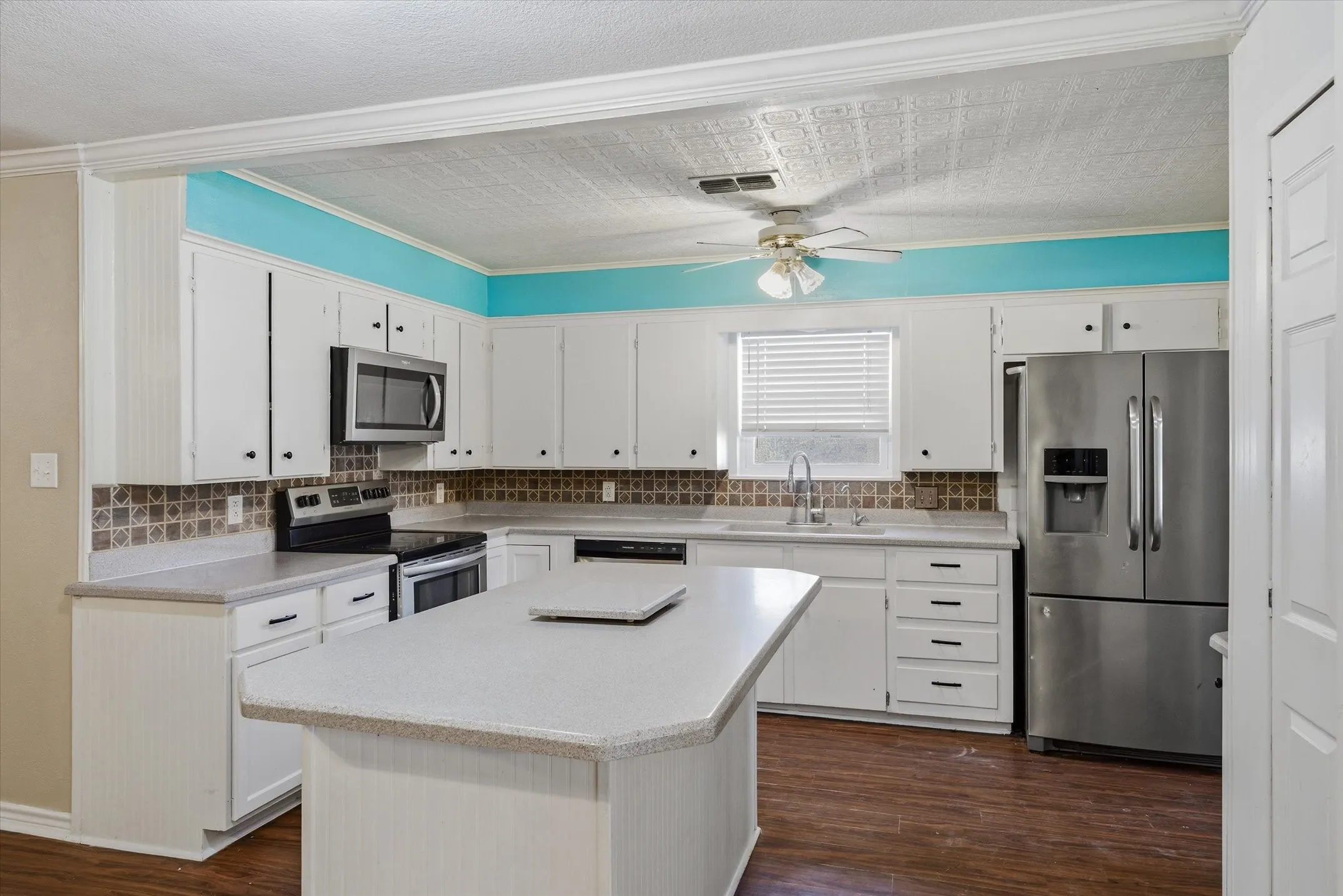 Kitchen featuring white cabinetry, light-toned countertops, stainless steel appliances, a center island, and wood-finish flooring