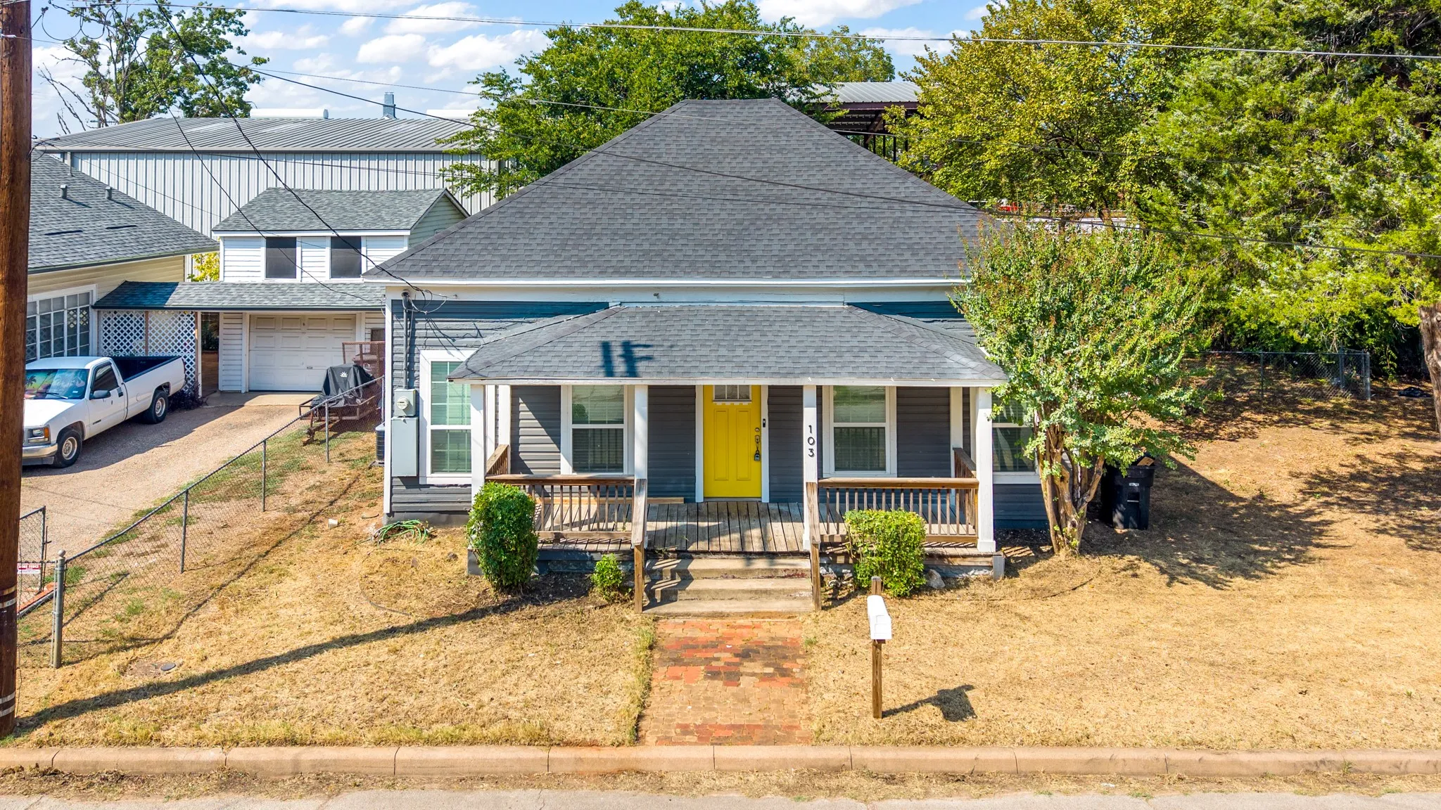 Exterior featuring gray siding, a dark shingle roof, a yellow front door, and a covered porch with wood railings