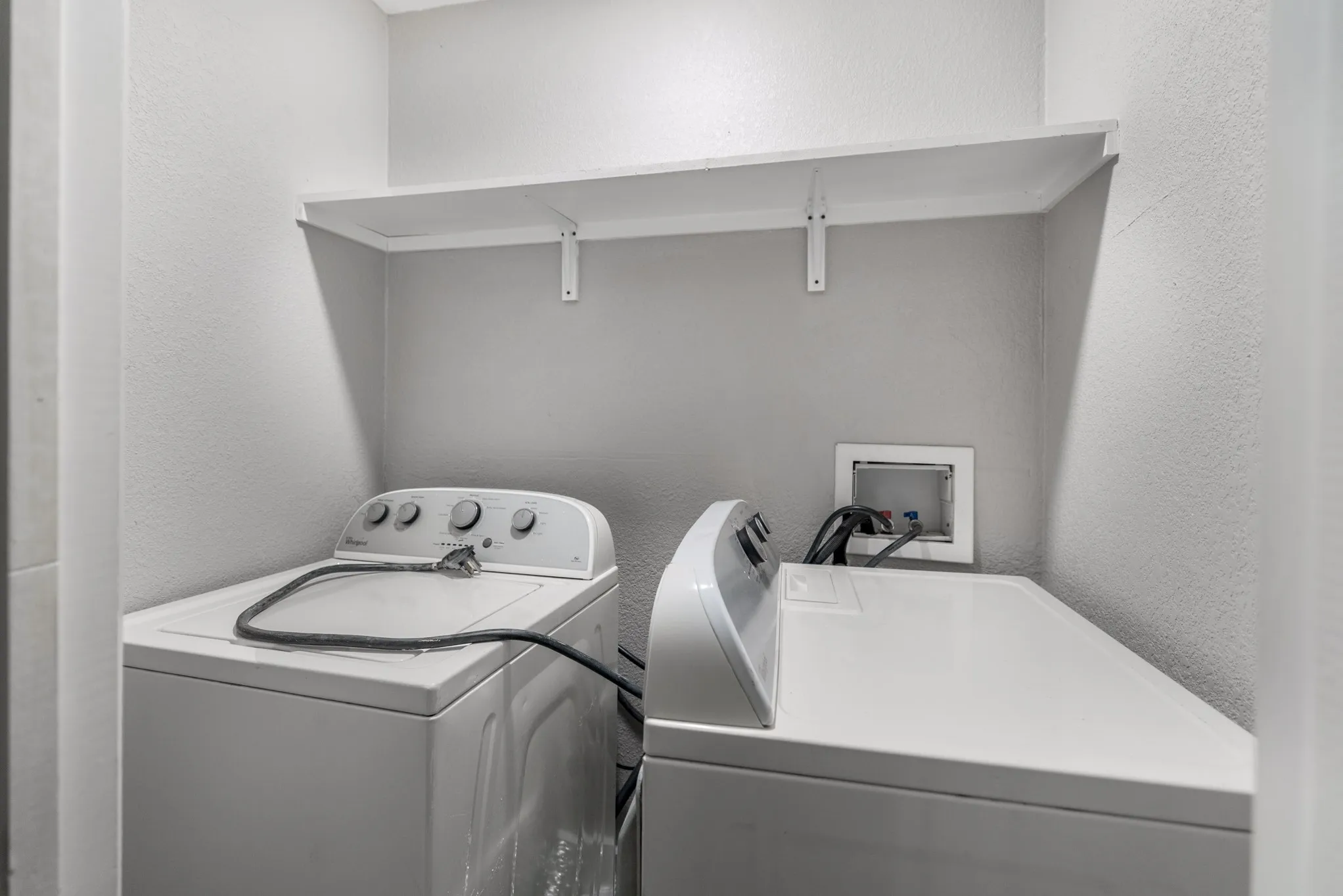 Laundry area featuring a top-load washer, front-load dryer, and an upper storage shelf