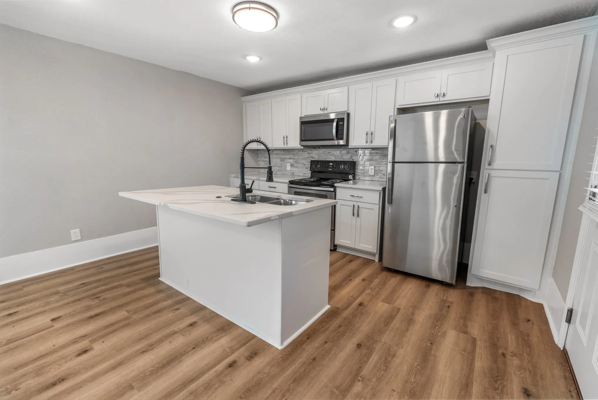 Kitchen featuring a central island with countertop seating, stainless steel appliances, white cabinetry, and wood-finish flooring