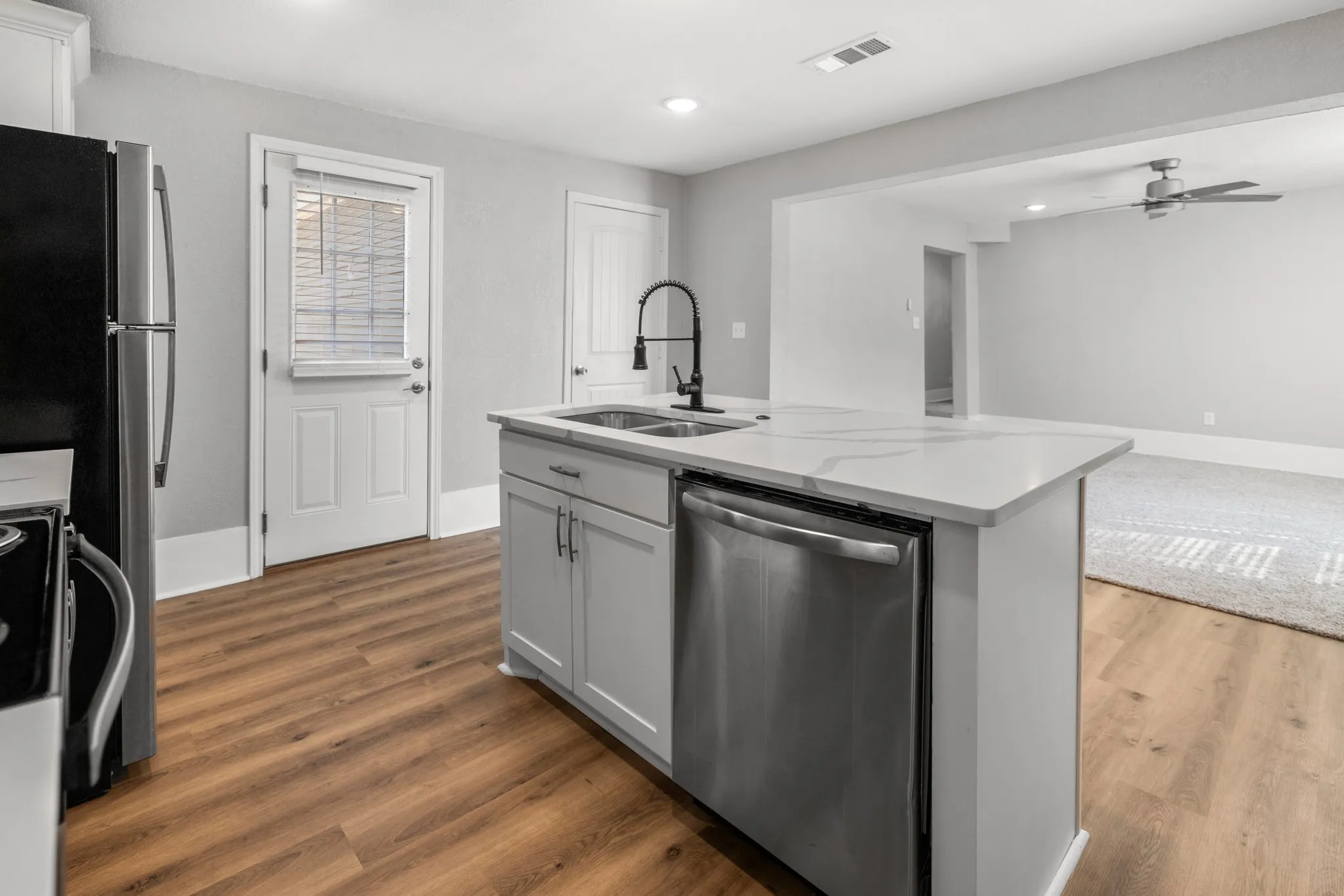 Kitchen featuring wood-finish flooring, a center island with a white countertop, stainless steel dishwasher, and a black faucet