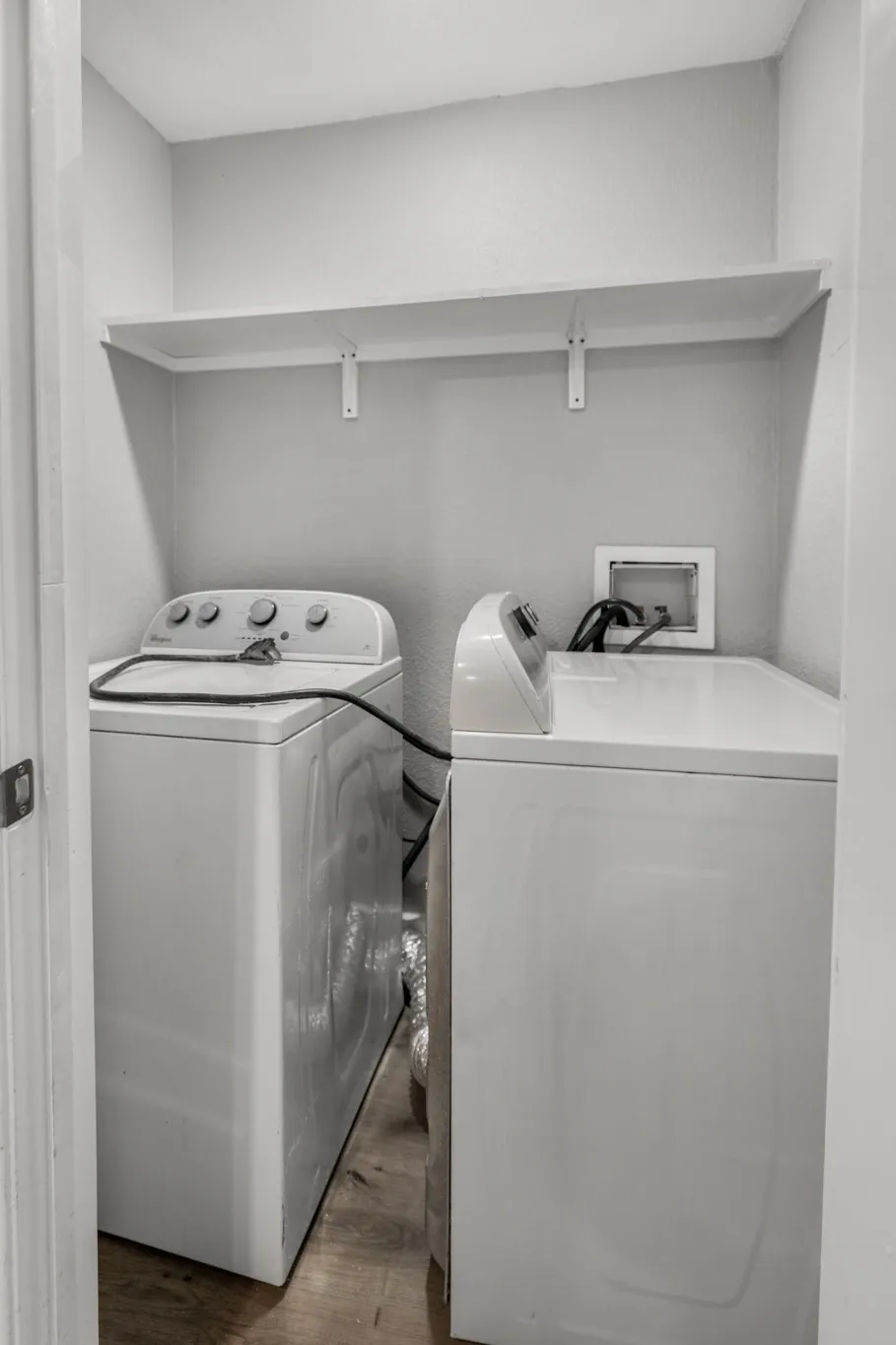 Laundry area featuring a top-load washing machine, a top-load clothes dryer, wood-finish flooring, and a wall-mounted white shelf