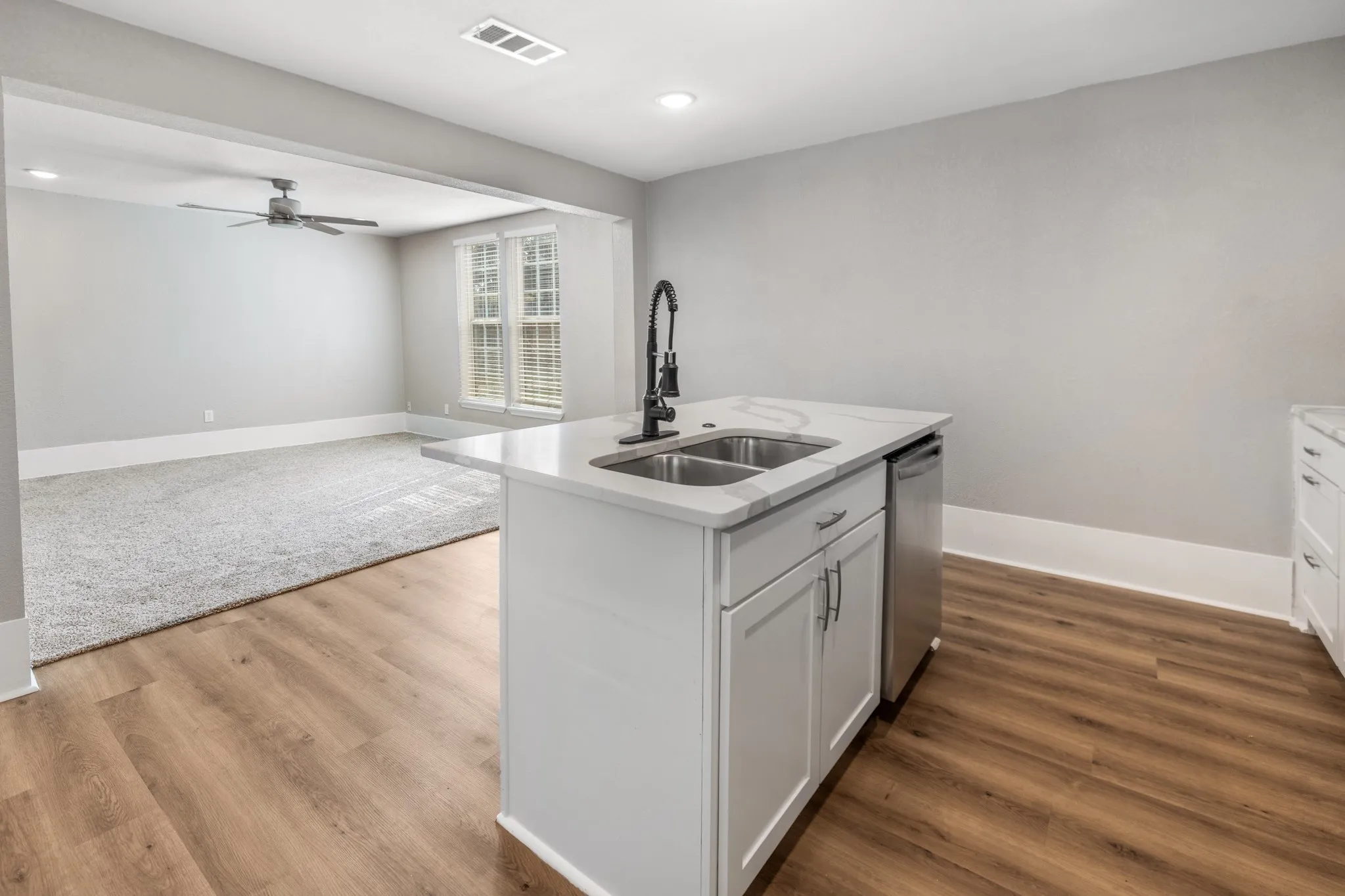 Kitchen island with white cabinetry, double basin sink, and integrated dishwasher