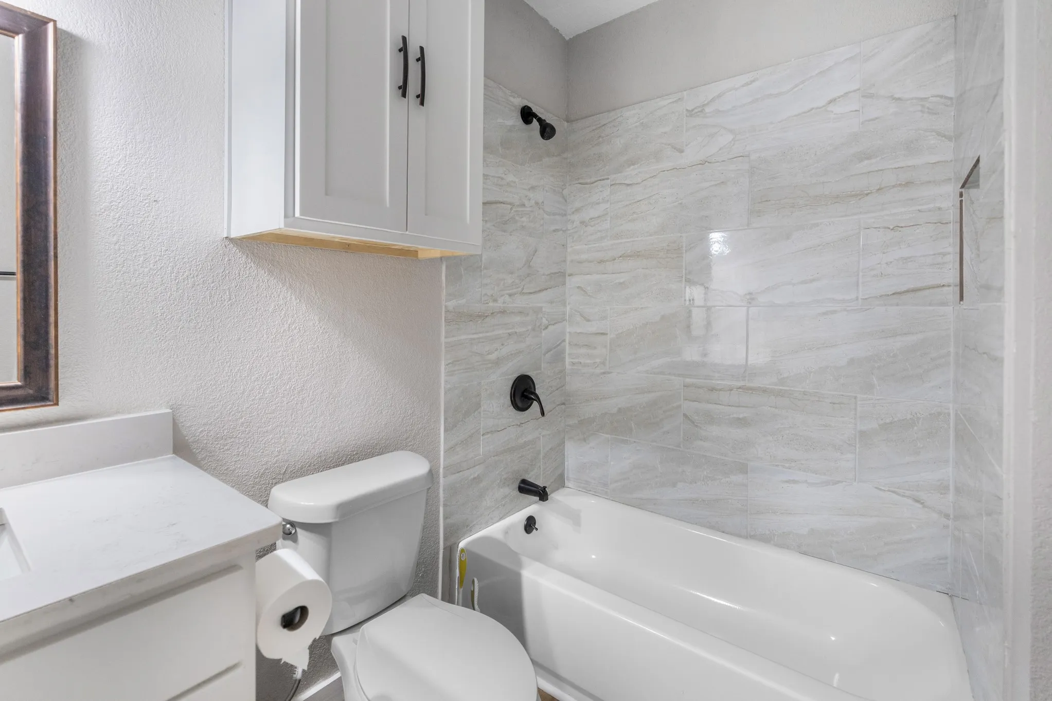 Bathroom featuring a white vanity with an integrated sink, a white bathtub, and a tiled shower surround with a built-in niche
