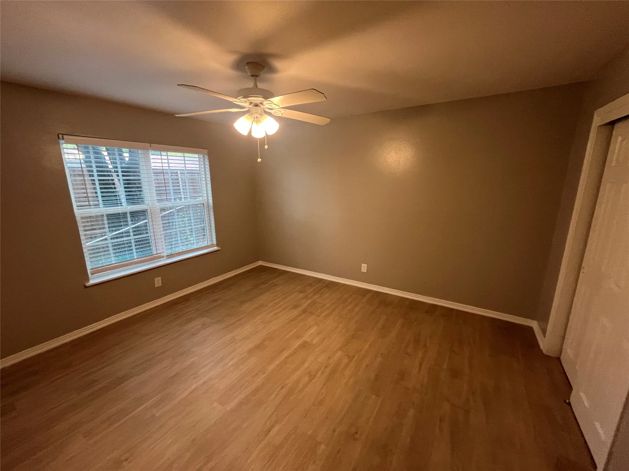 Wood-finish flooring, ceiling fan with integrated lighting, window with blinds, and neutral wall tones