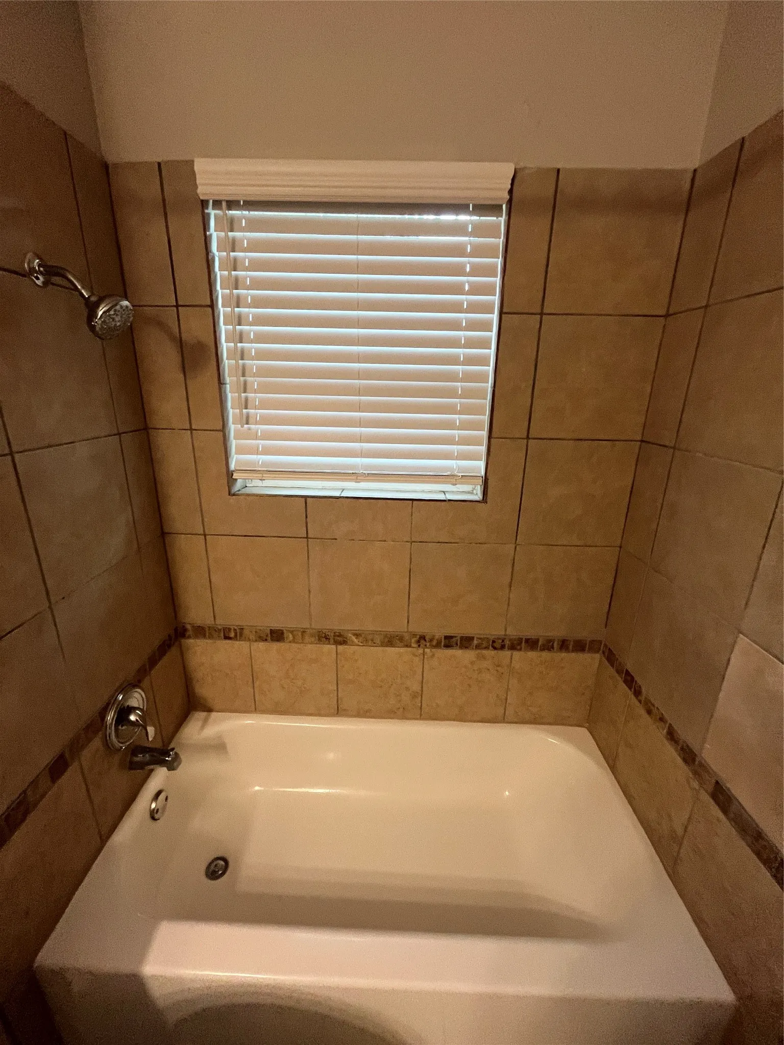 Bathtub with tiled surround, decorative tile accent band, and an integrated window with blinds