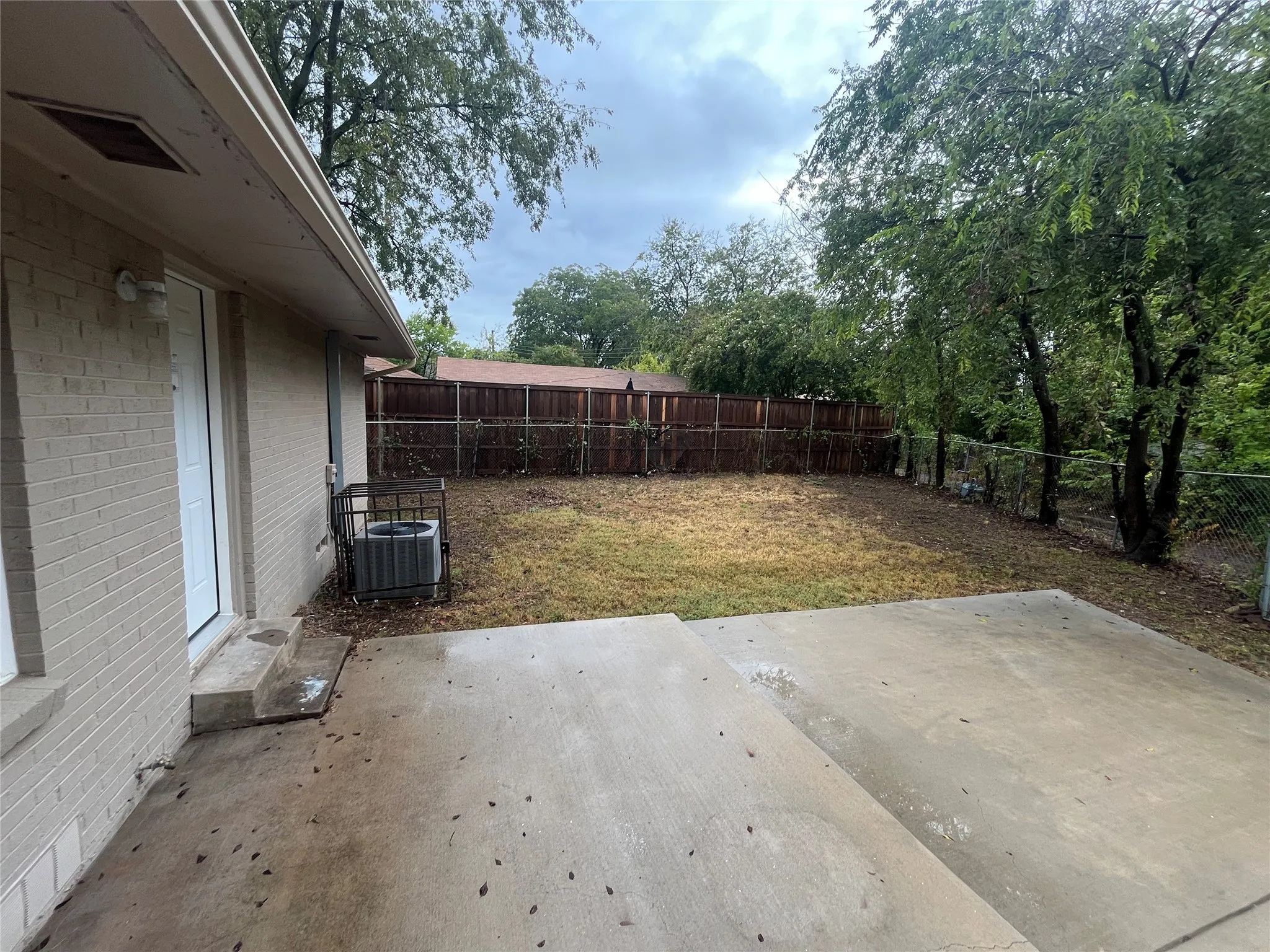 Expansive backyard featuring a concrete patio, mature trees, and a combination of chain-link and wood privacy fencing