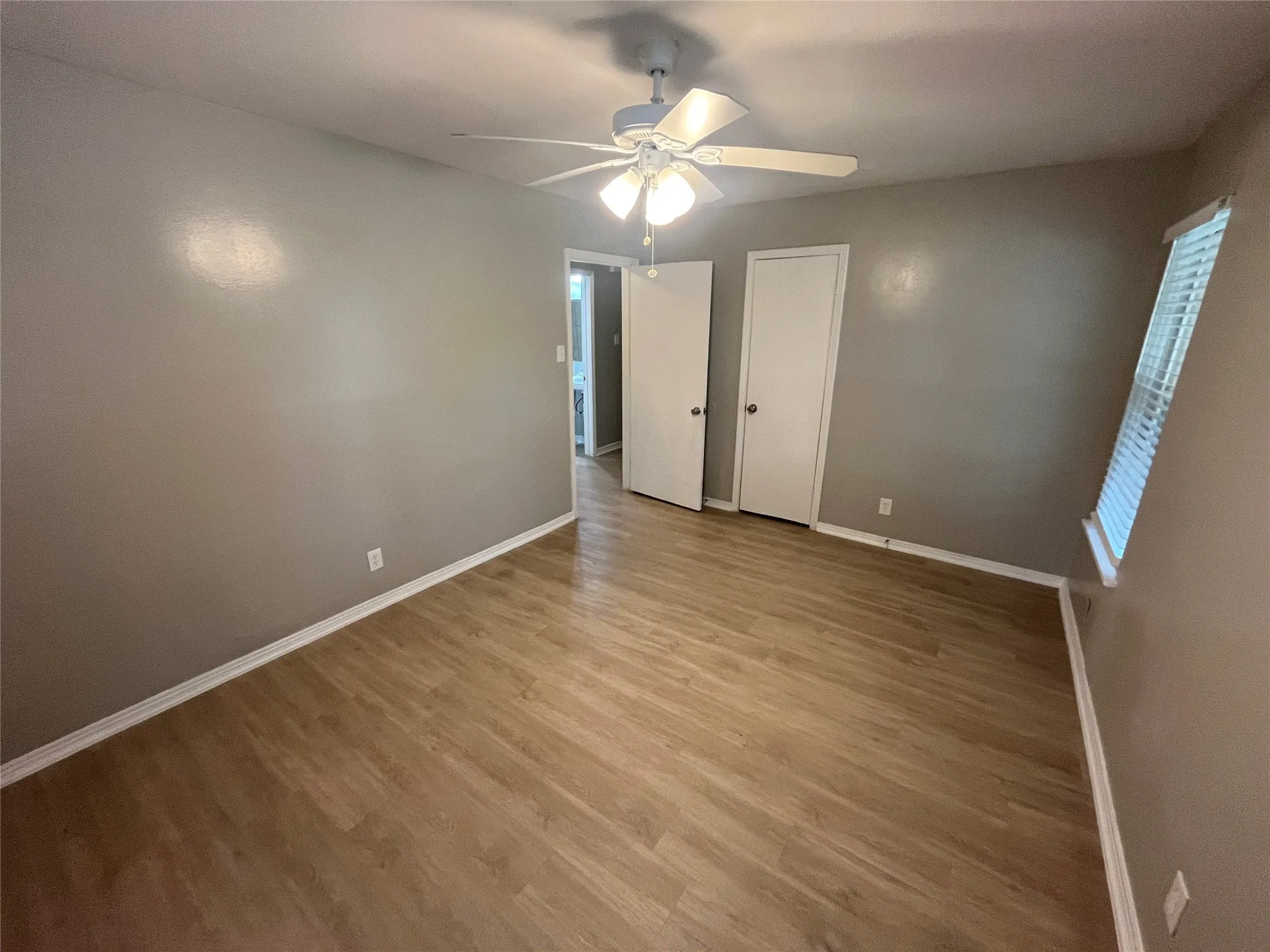 Wood-finish flooring, ceiling fan with integrated lighting, window with blinds, and neutral wall tones