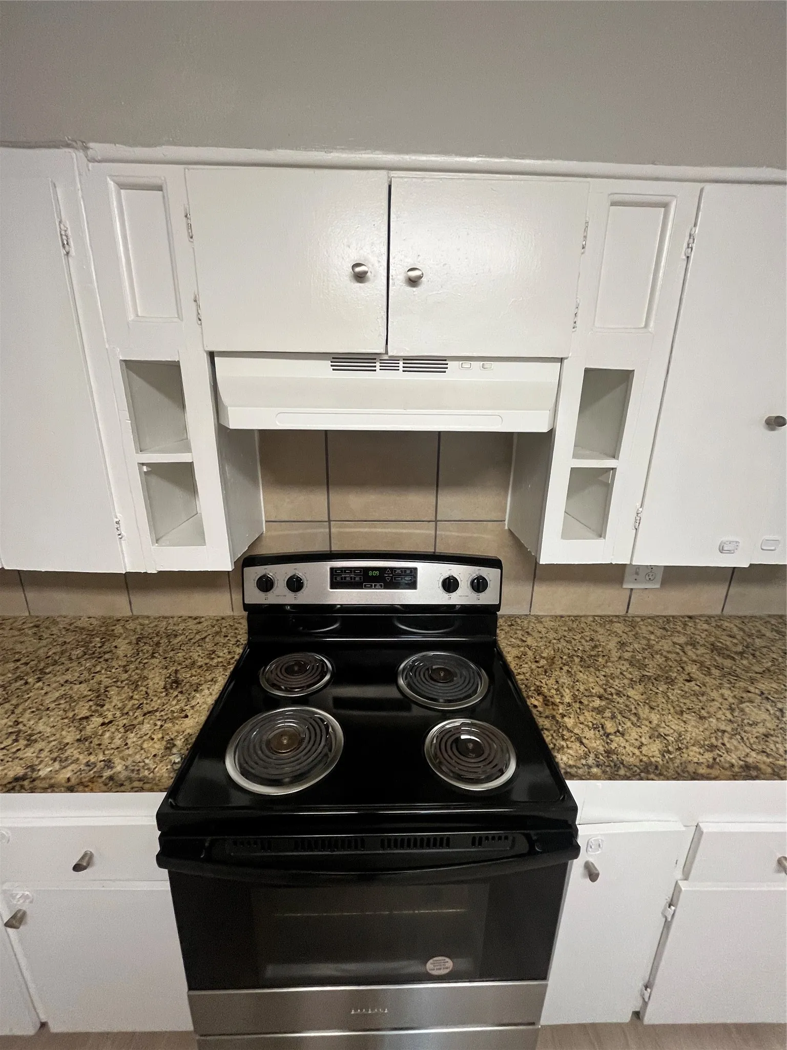 Stainless steel range, white cabinetry, granite-finish countertops, tiled backsplash, and integrated range hood